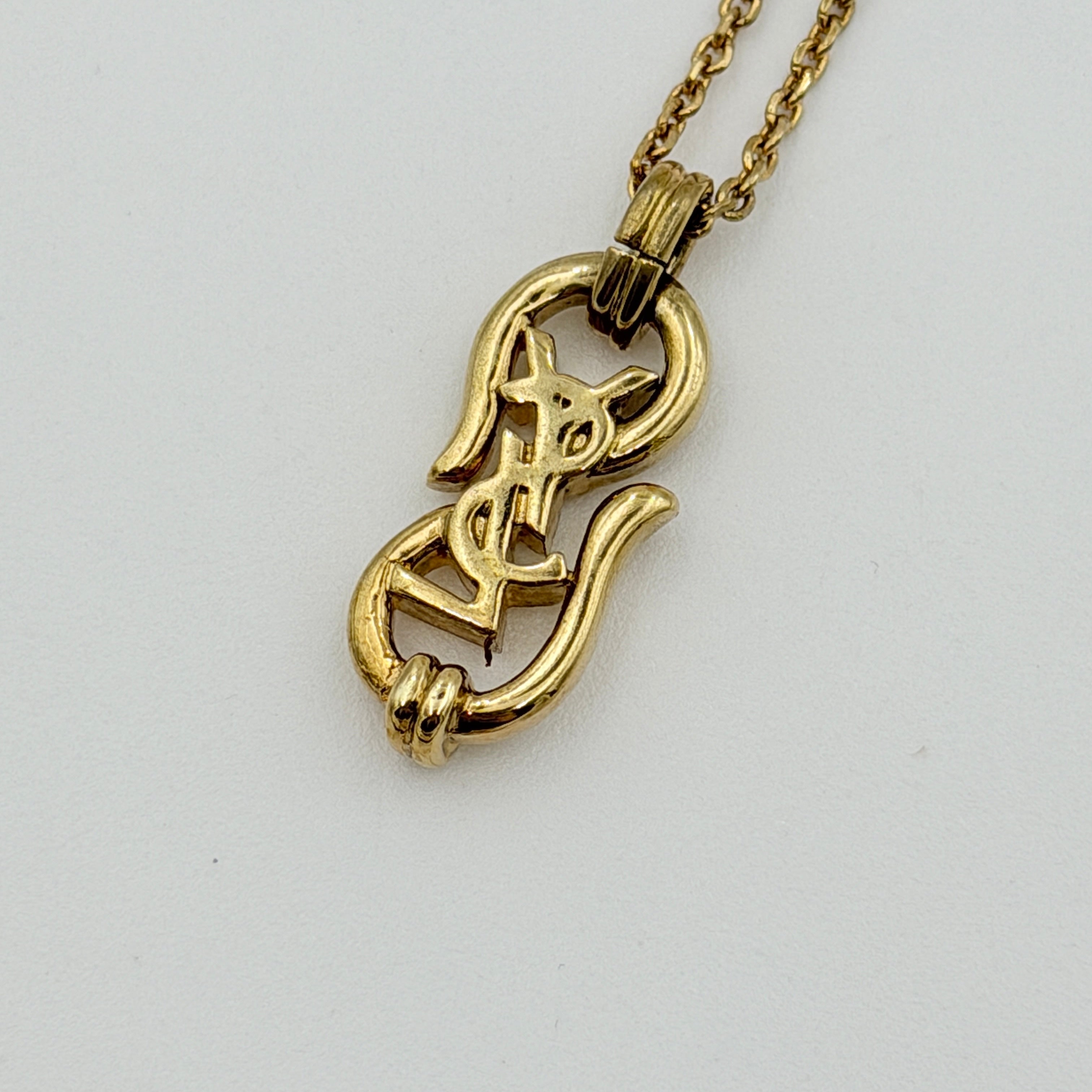 Saint Laurent Cassandre Logo Necklace in gold metal with signature YSL pendant displayed on a necklace stand.