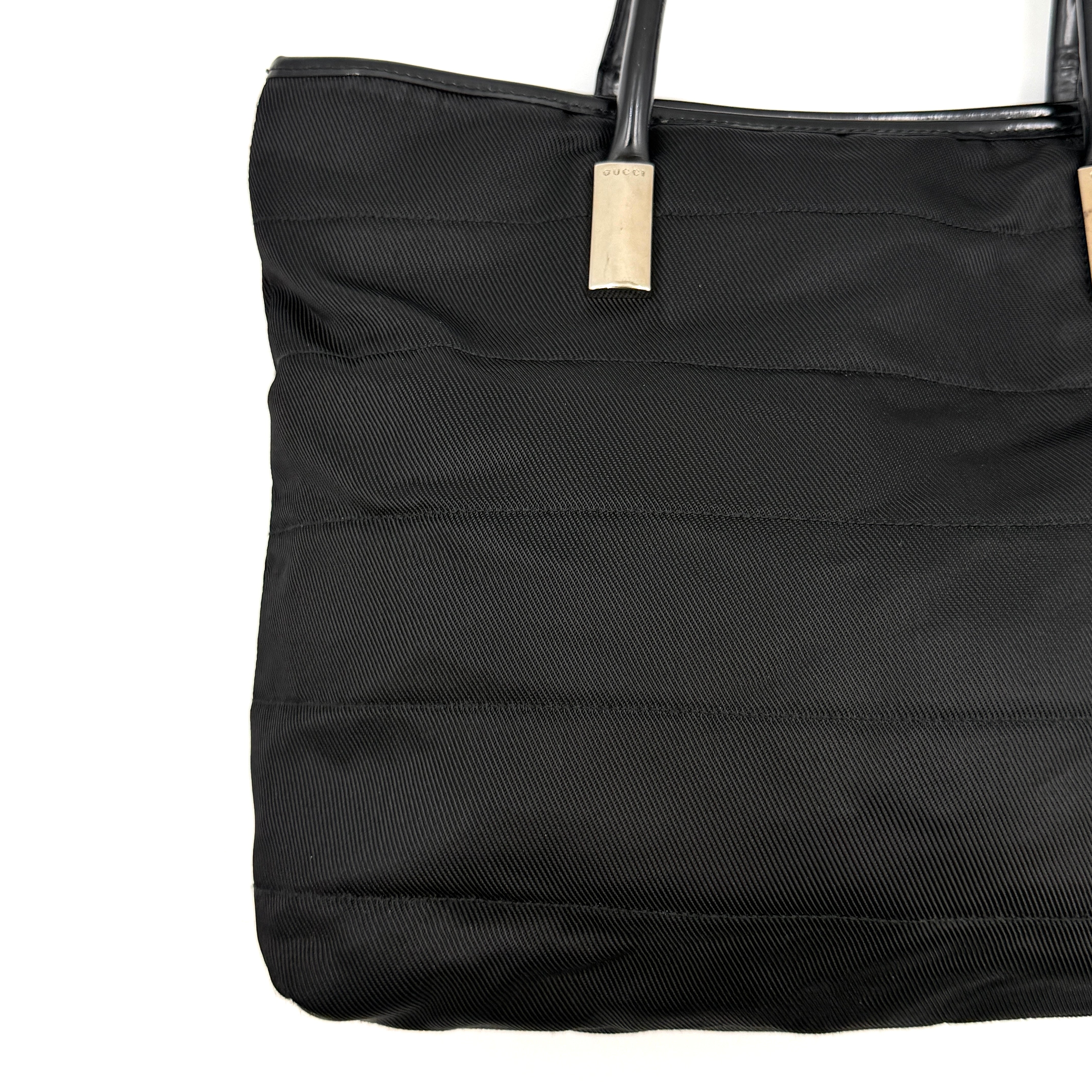 A classic black Gucci nylon tote bag with leather handles and gold-tone hardware displayed upright against a clean background.