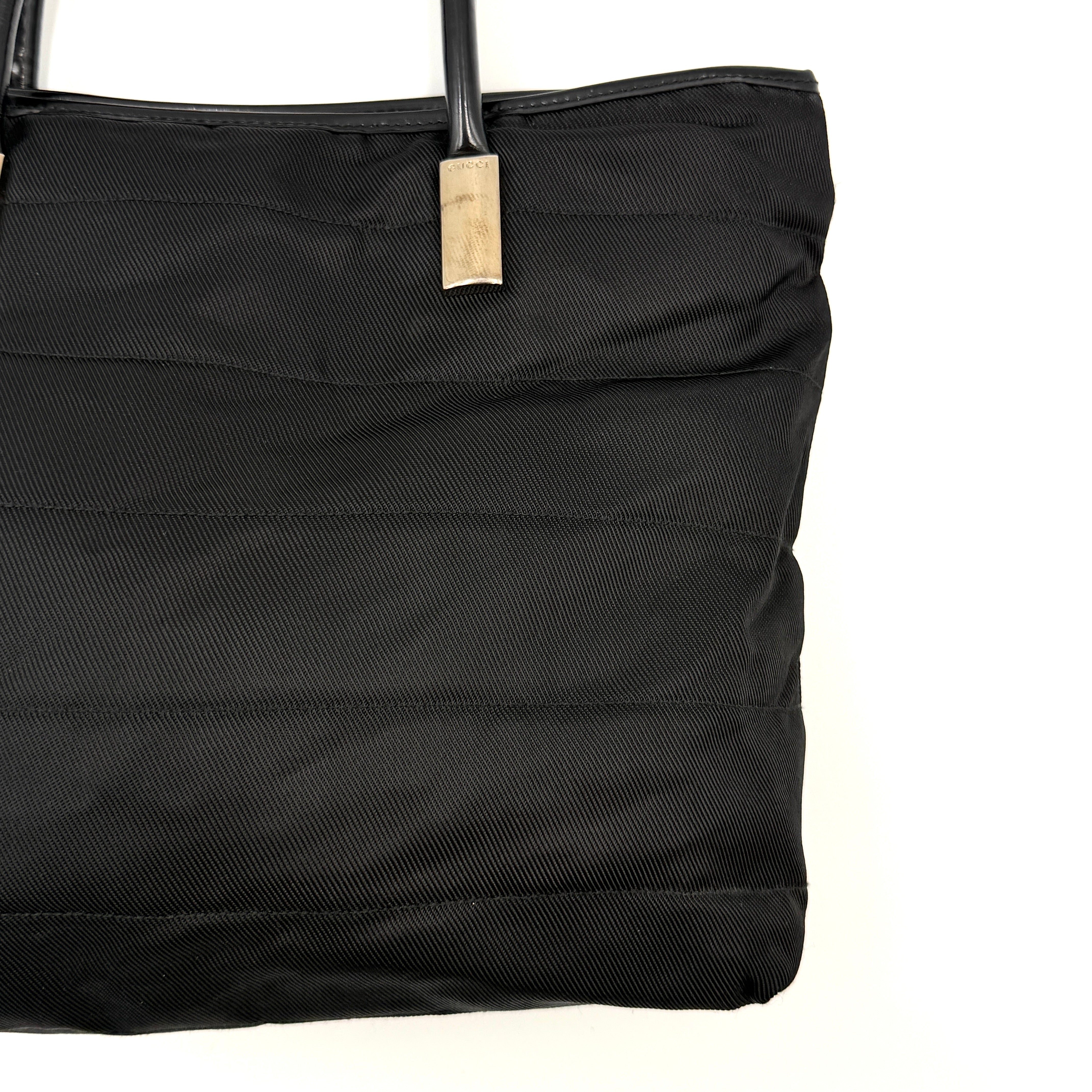 A classic black Gucci nylon tote bag with leather handles and gold-tone hardware displayed upright against a clean background.