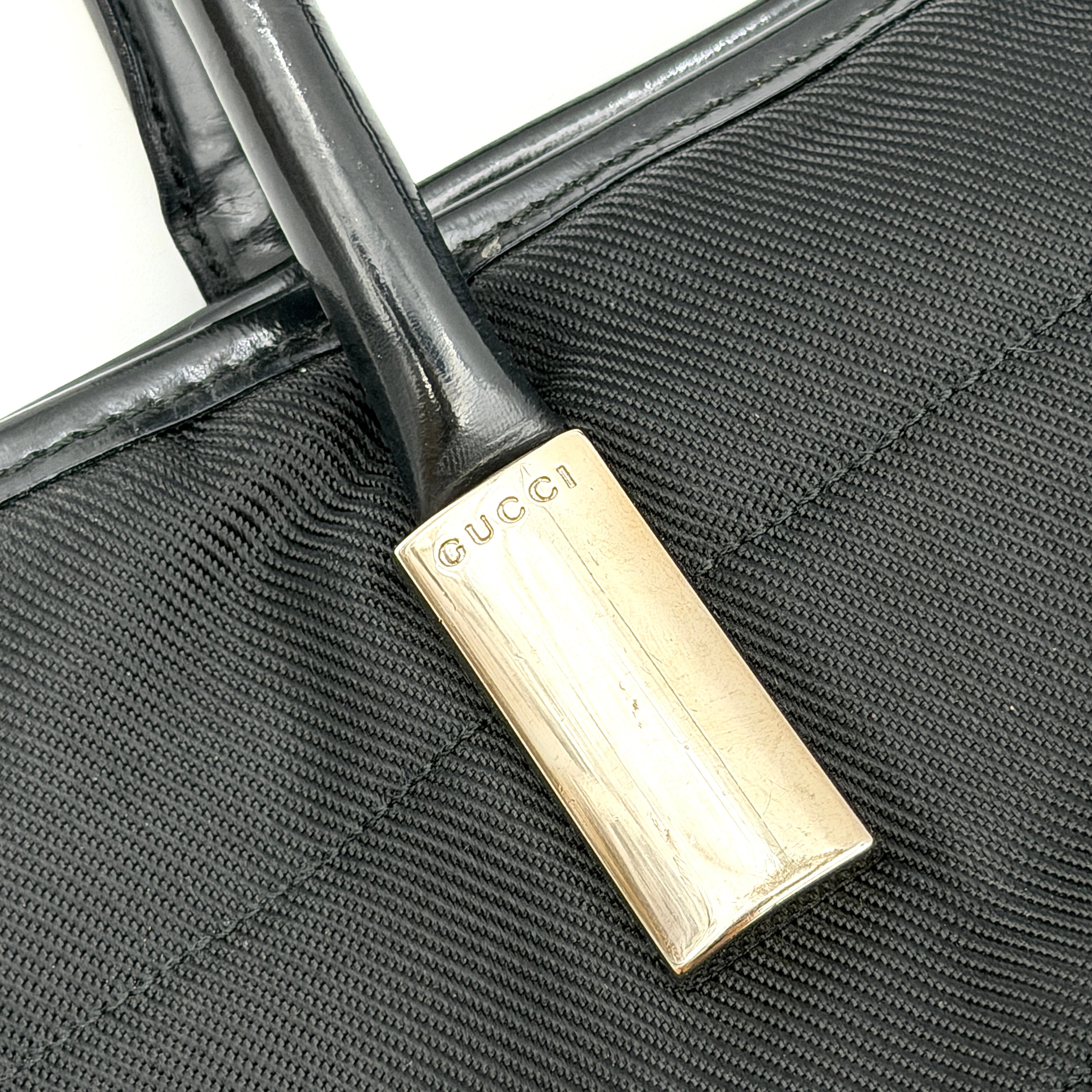 A classic black Gucci nylon tote bag with leather handles and gold-tone hardware displayed upright against a clean background.