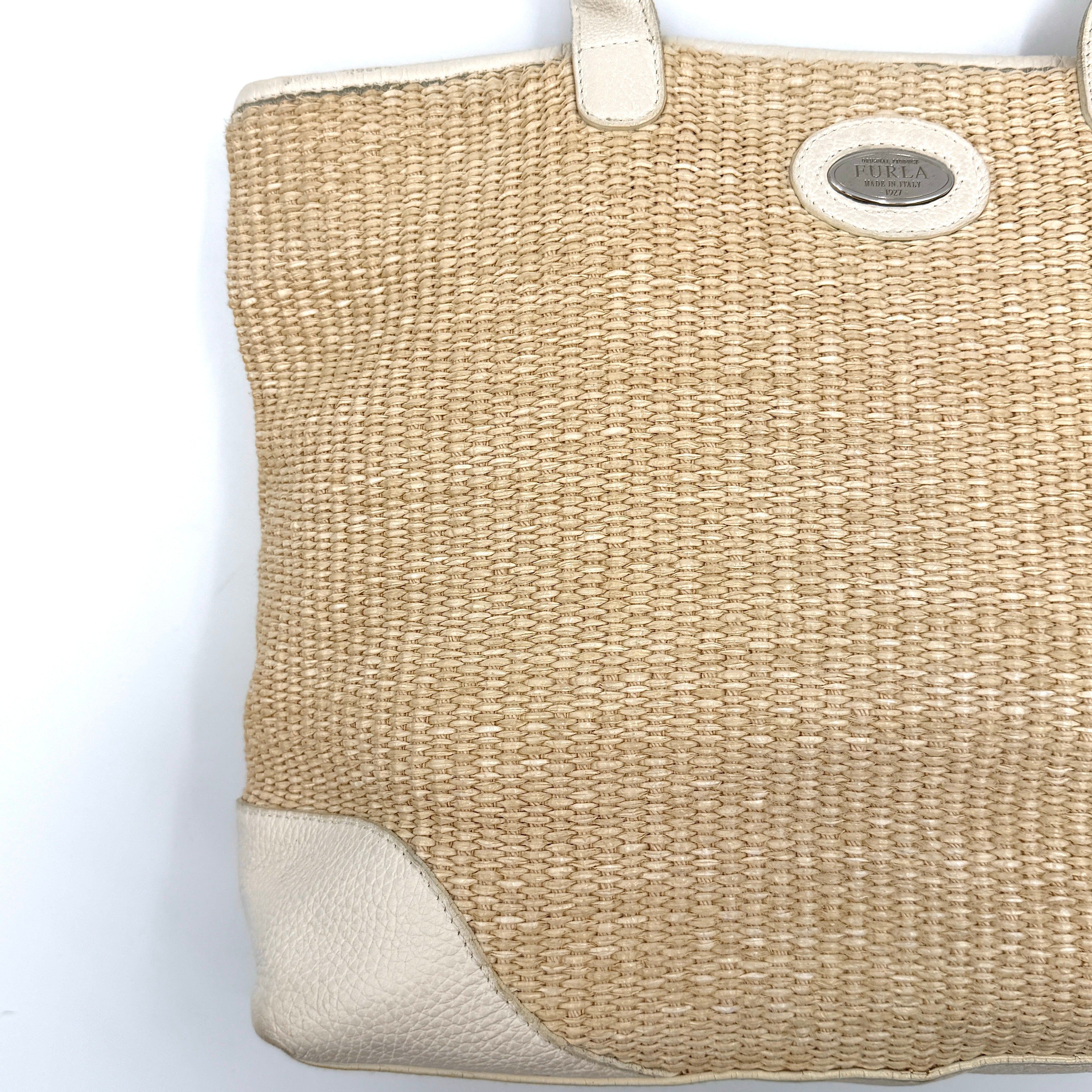 Furla beige woven straw tote bag with off-white leather handles and corners, featuring a silver oval logo plaque.