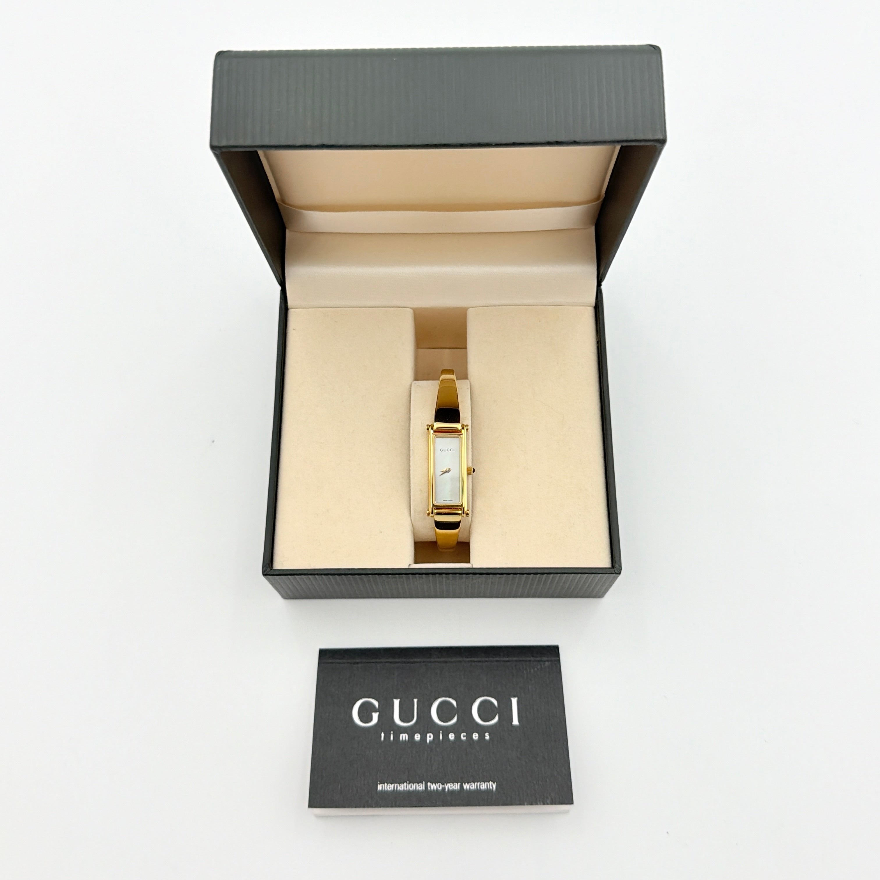 Gucci 1500L gold-tone quartz watch with white rectangular dial, displayed in box with warranty card.