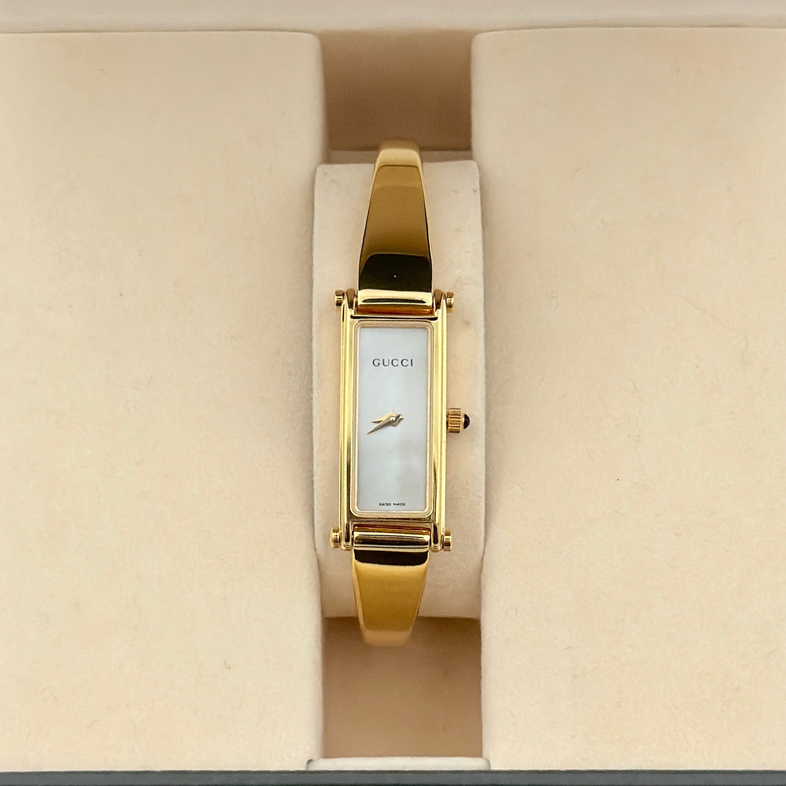 Gucci 1500L gold-tone quartz watch with white rectangular dial, displayed in box with warranty card.