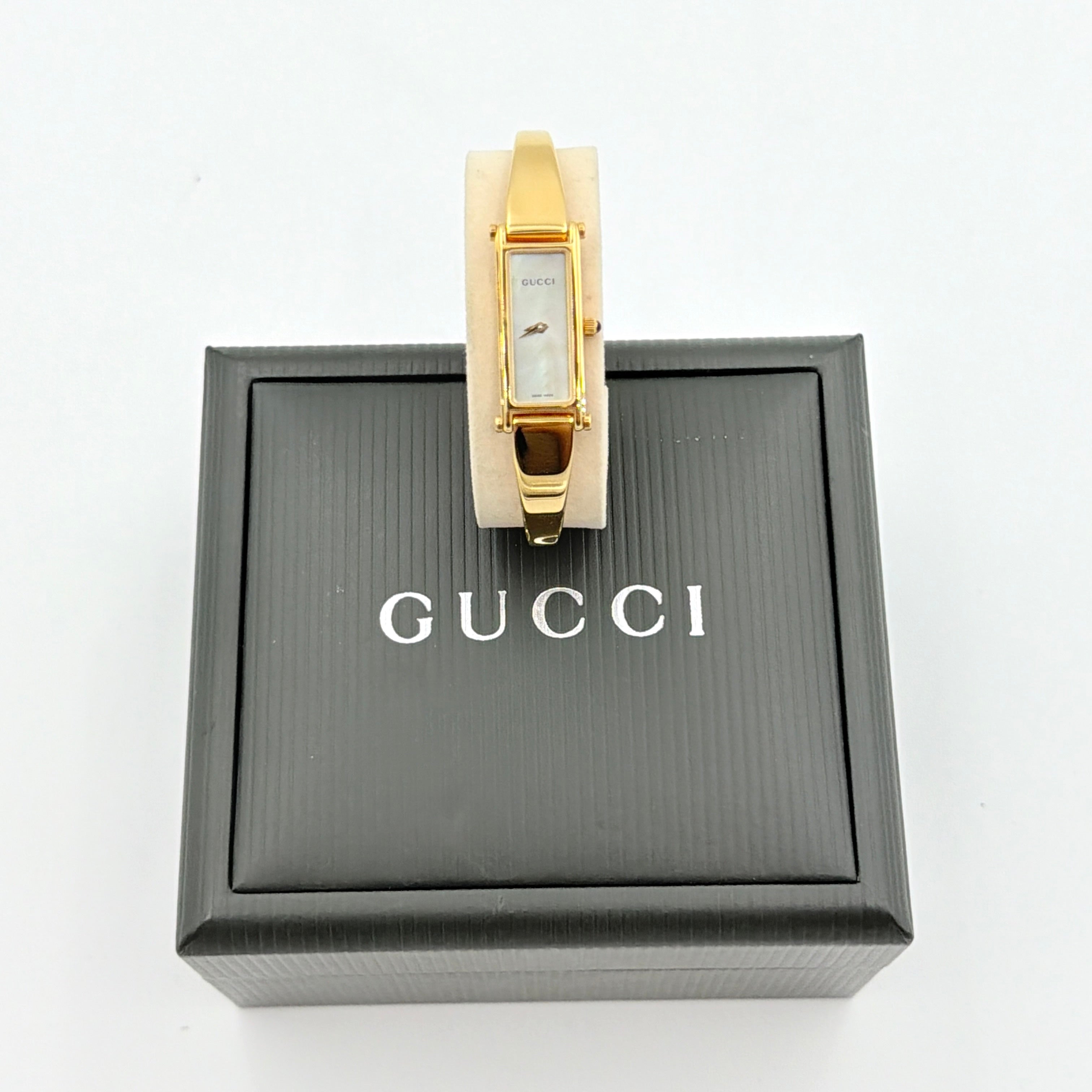 Gucci 1500L gold-tone quartz watch with white rectangular dial, displayed in box with warranty card.