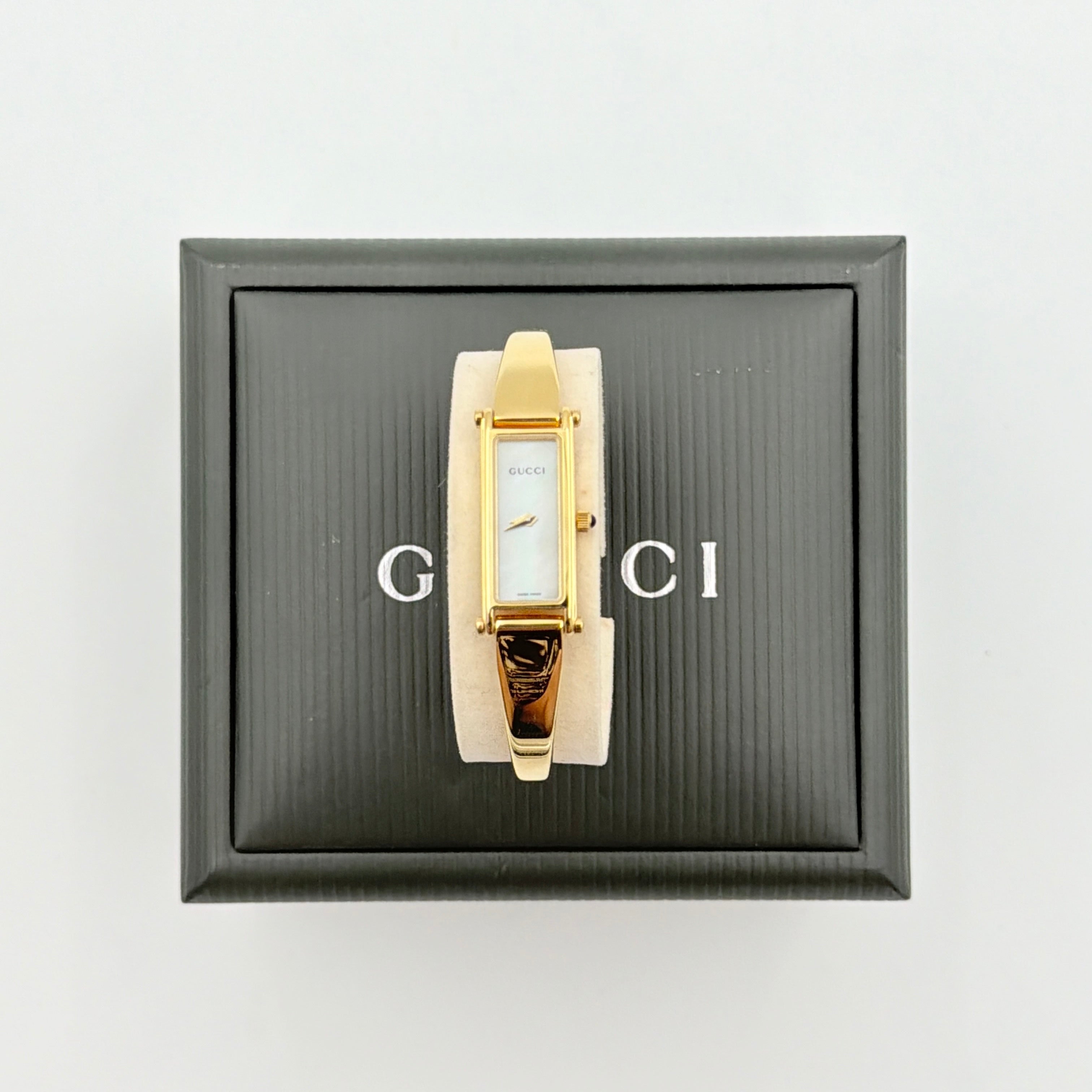 Gucci 1500L gold-tone quartz watch with white rectangular dial, displayed in box with warranty card.