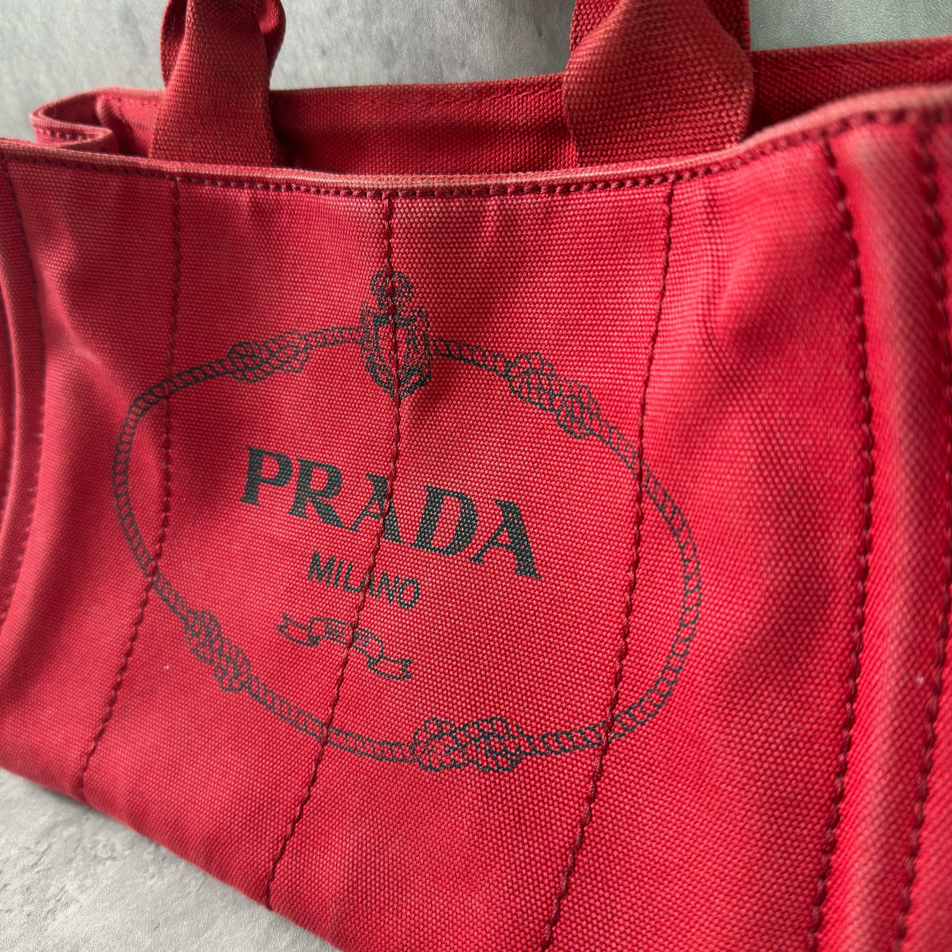 Prada Canapa Tote Bag in red canvas with black logo embroidery, featuring a structured silhouette and dual top handles for effortless style.