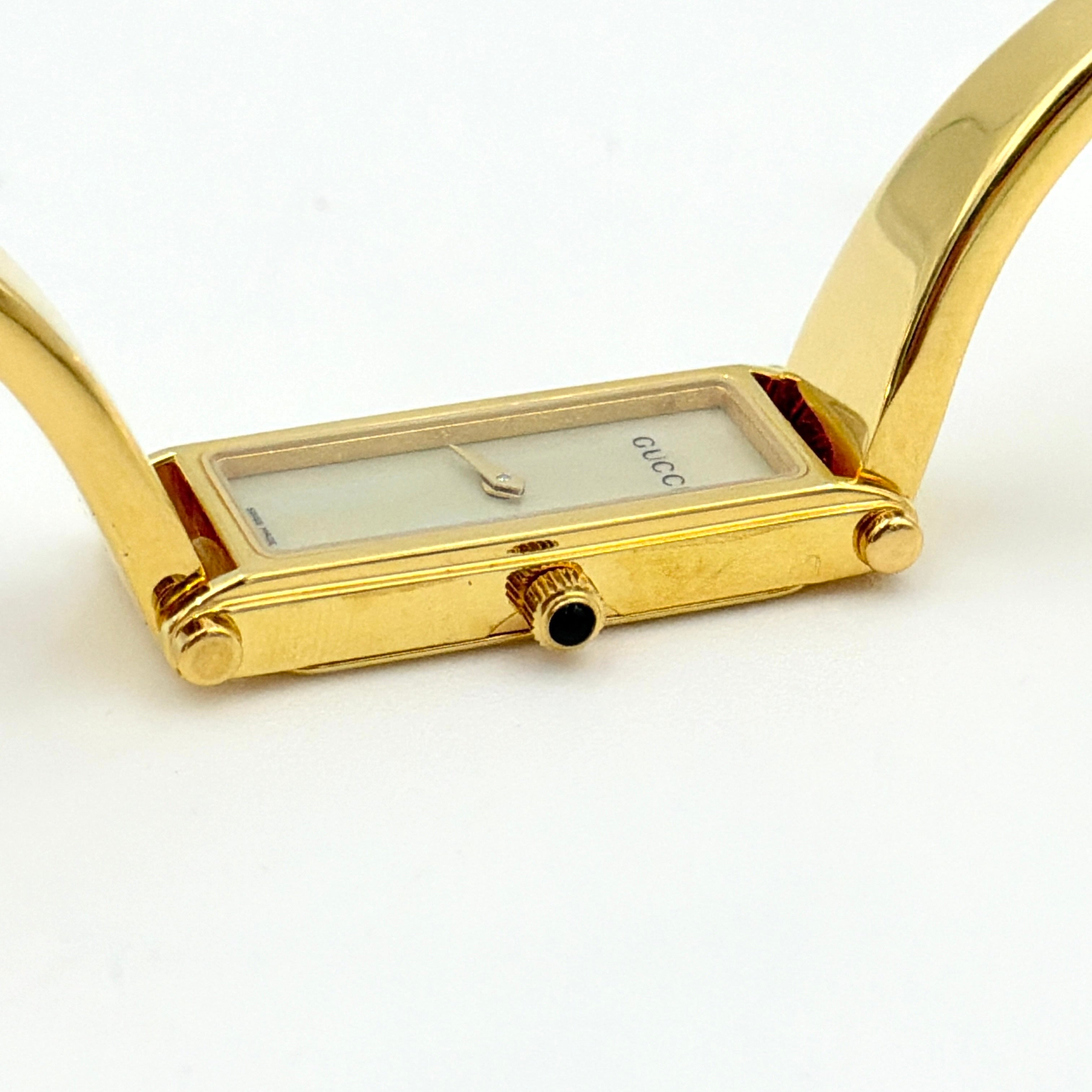 Gucci 1500L gold-tone quartz watch with white rectangular dial, displayed in box with warranty card.