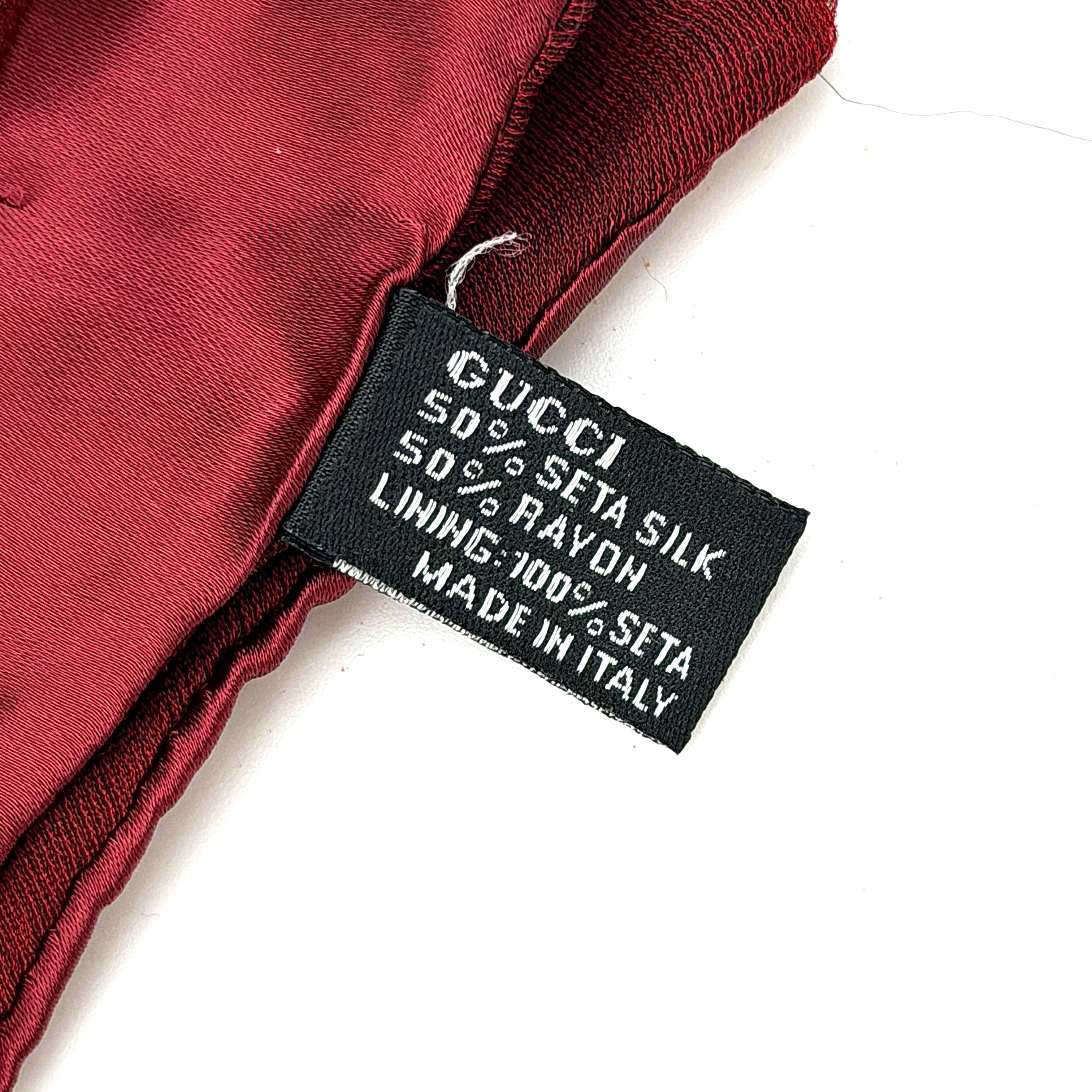 A maroon Gucci silk scarf with a tonal geometric jacquard pattern and a lustrous silk border, elegantly displayed to highlight its texture.