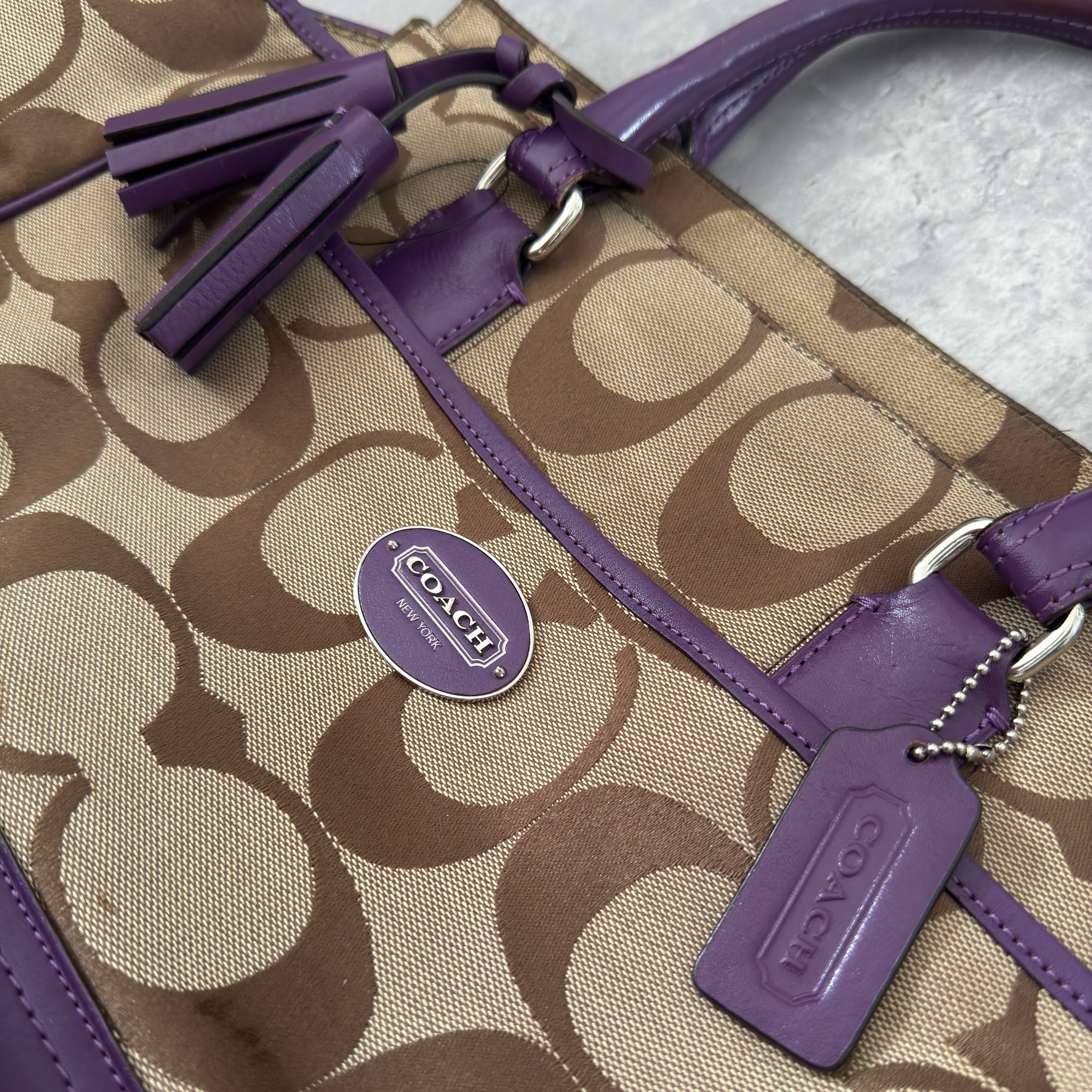 Coach Signature Legacy Candace Carry-All handbag in beige coated canvas with monogram print, purple leather trim, silver-tone hardware, and tassel details.
