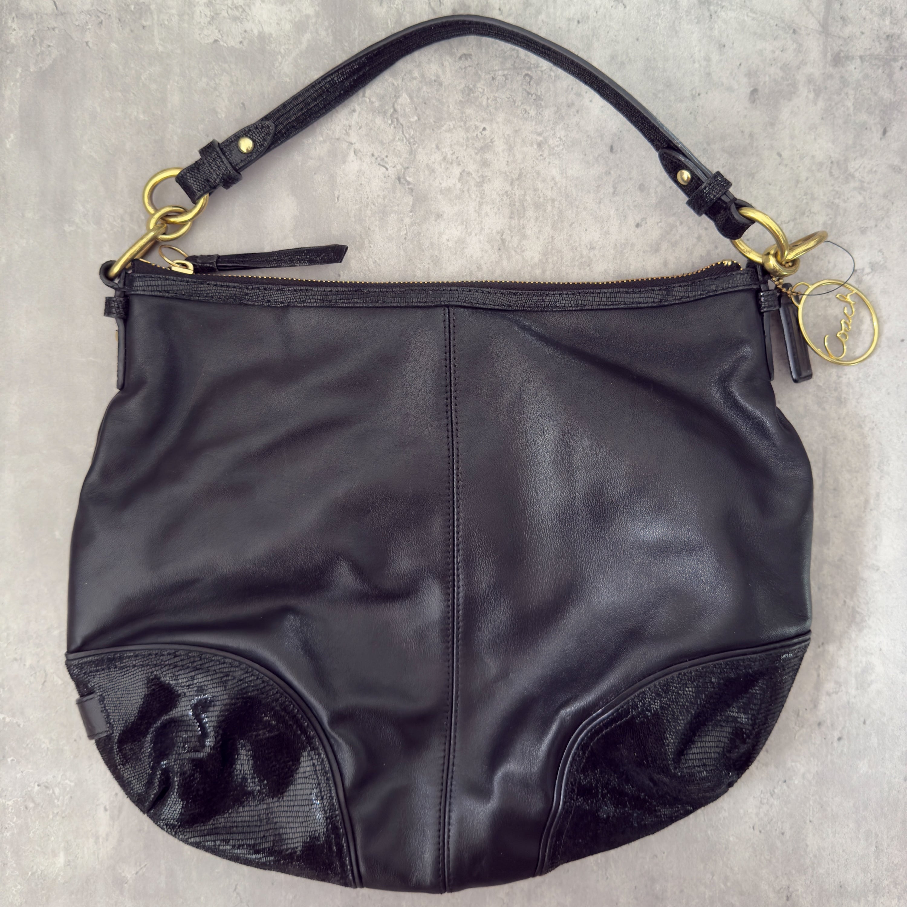 Coach Signature Cursive Logo Shoulder Bag in black leather with gold-tone hardware, featuring a spacious fabric-lined interior and signature Coach charm.