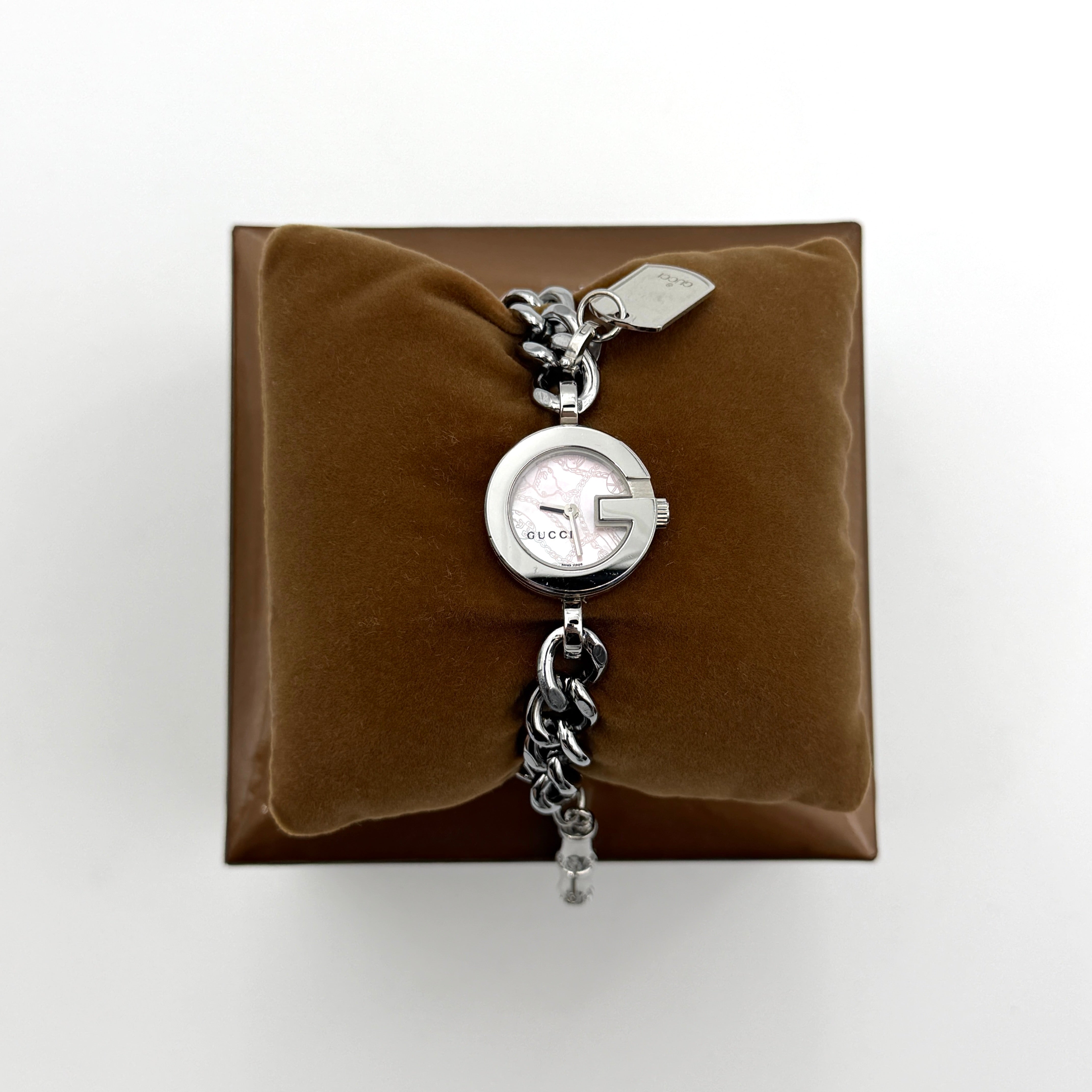 Gucci 107 G Charm Bracelet Watch with silver chunky chain and pink dial, styled on a brown cushion with original Gucci box.