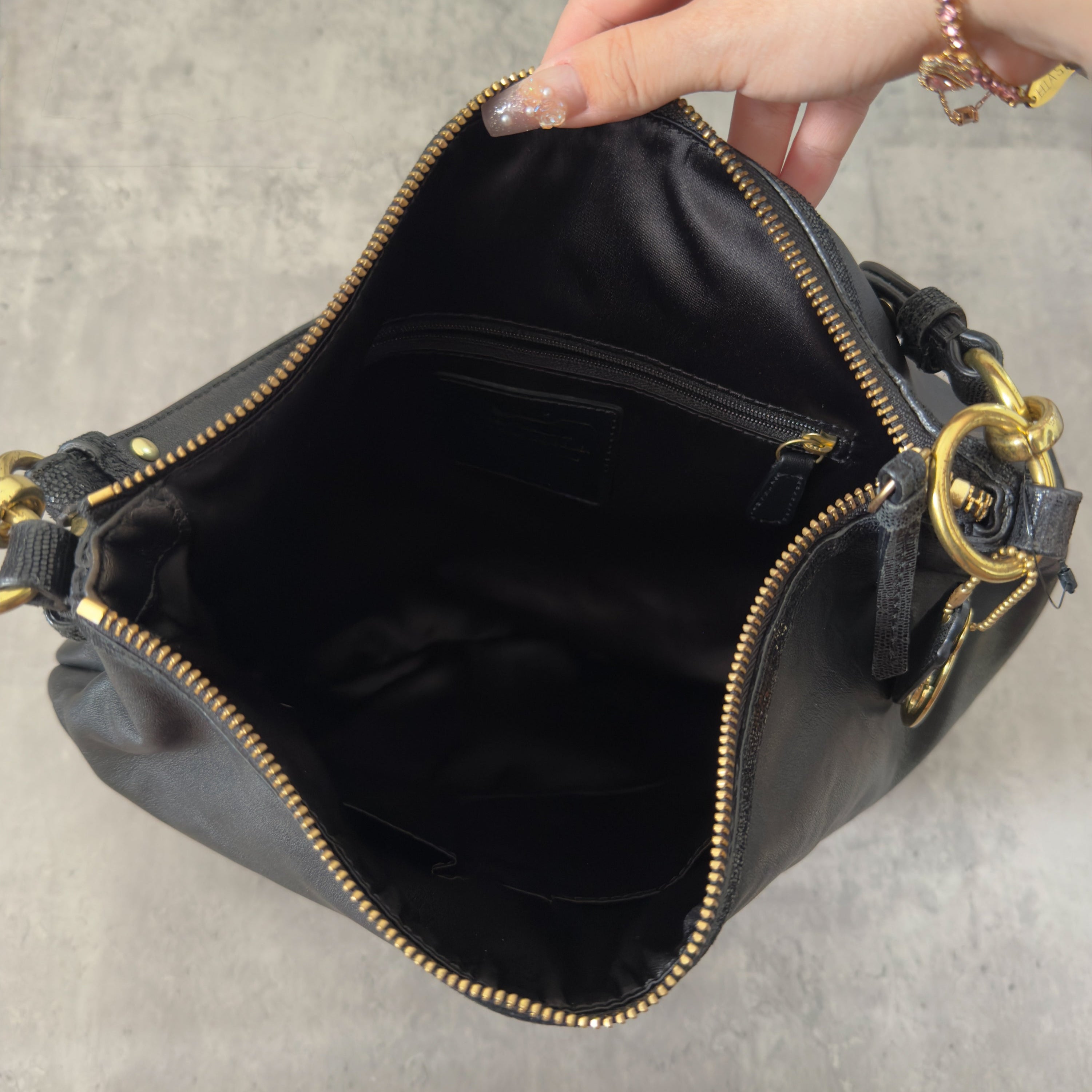 Coach Signature Cursive Logo Shoulder Bag in black leather with gold-tone hardware, featuring a spacious fabric-lined interior and signature Coach charm.