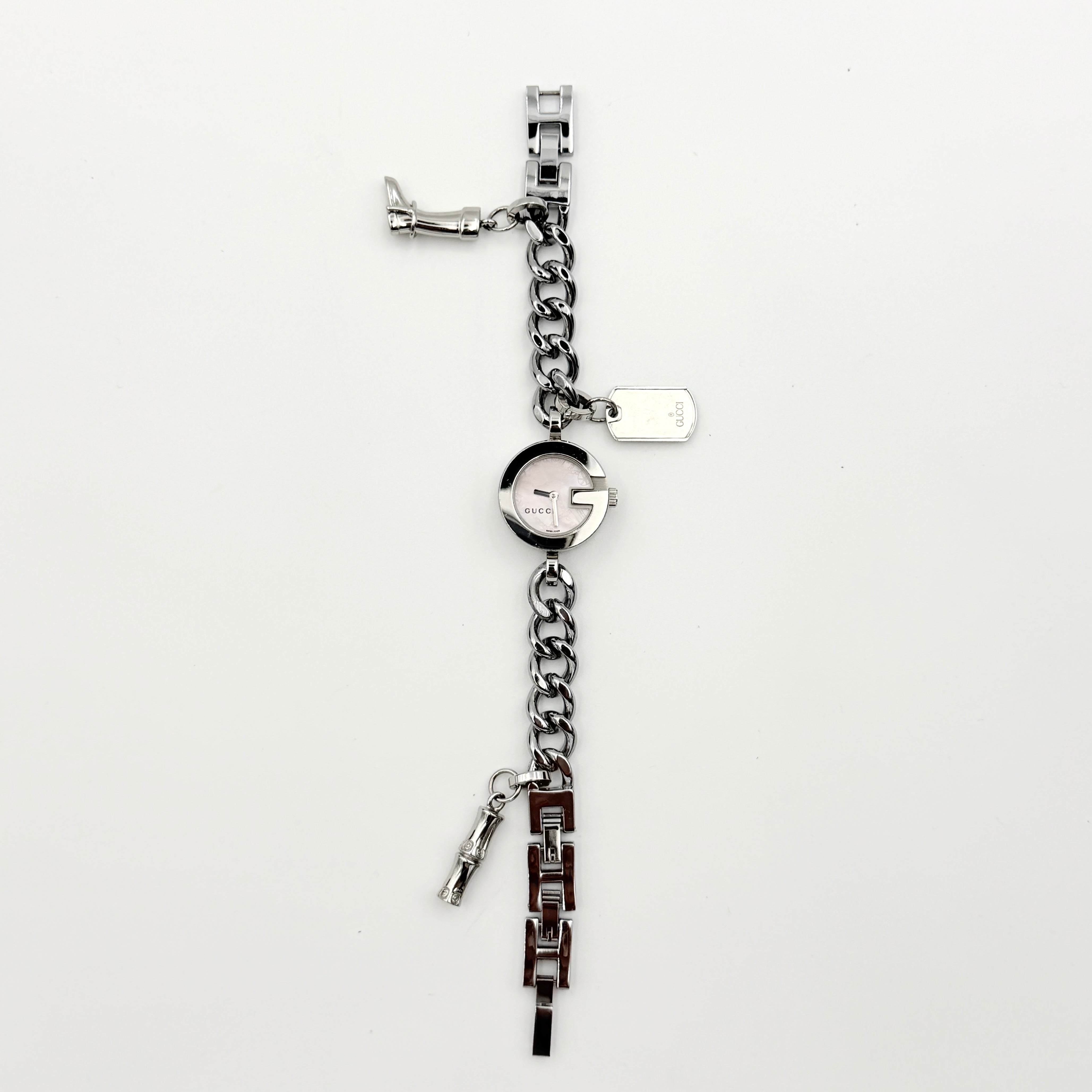 Gucci 107 G Charm Bracelet Watch with silver chunky chain and pink dial, styled on a brown cushion with original Gucci box.
