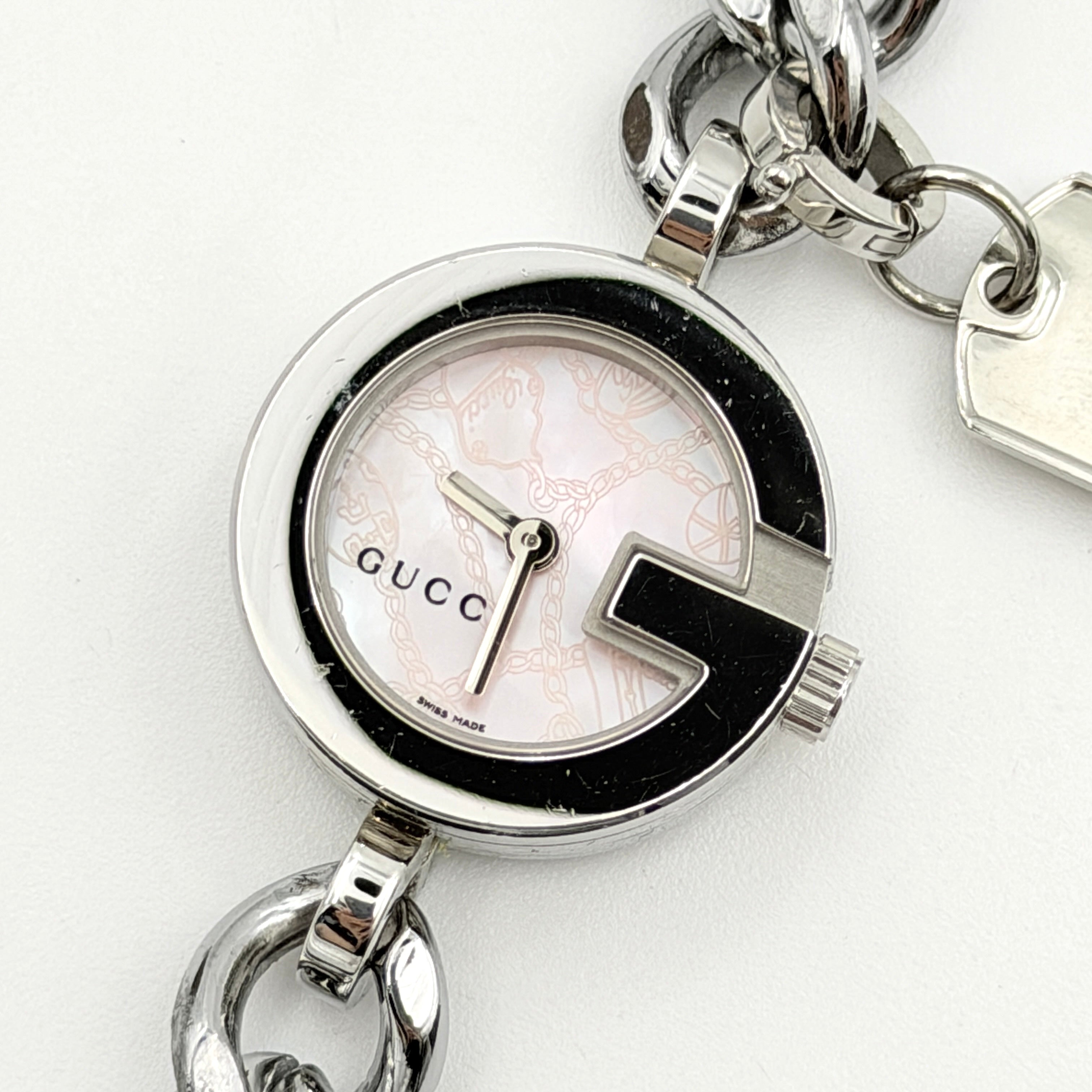Gucci 107 G Charm Bracelet Watch with silver chunky chain and pink dial, styled on a brown cushion with original Gucci box.
