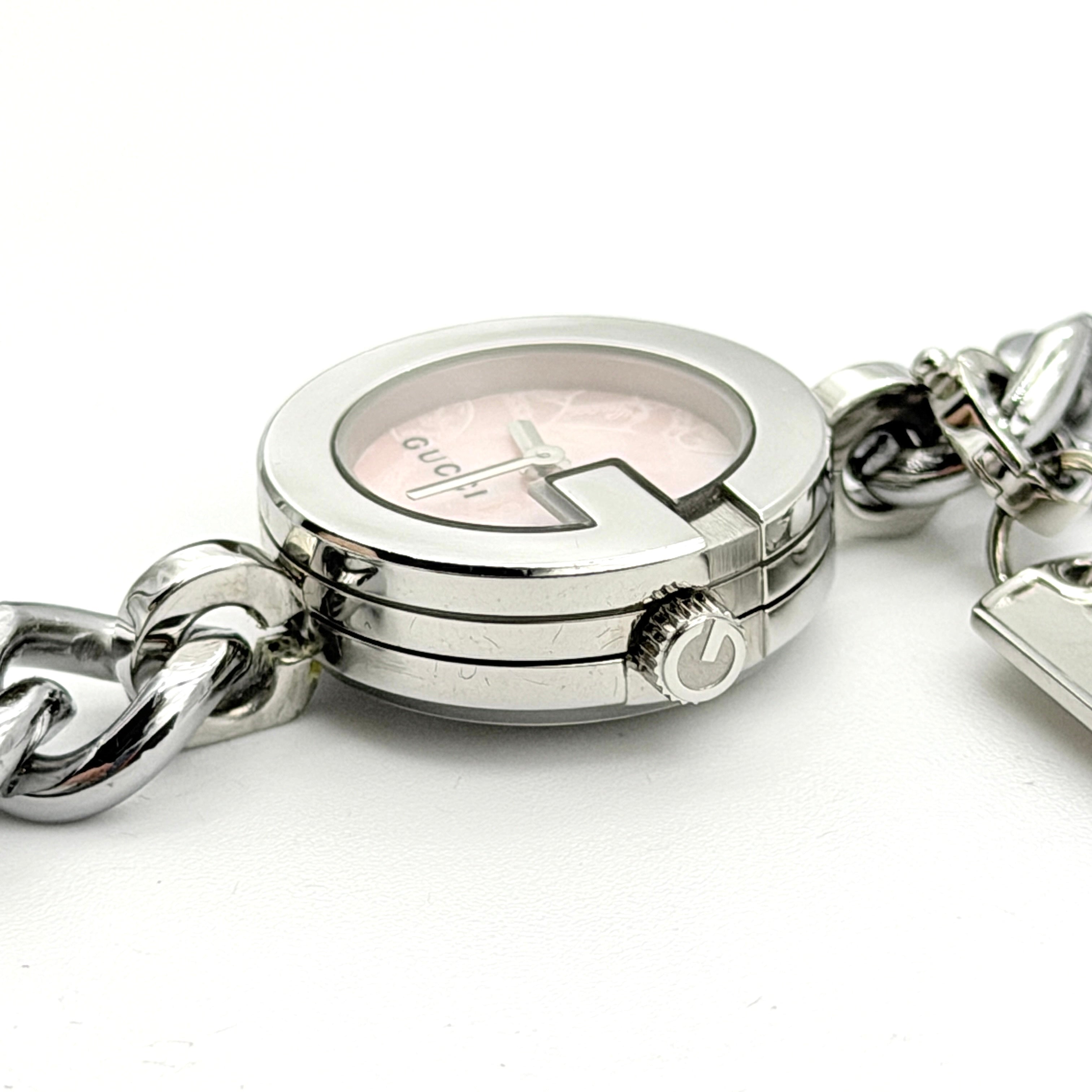 Gucci 107 G Charm Bracelet Watch with silver chunky chain and pink dial, styled on a brown cushion with original Gucci box.