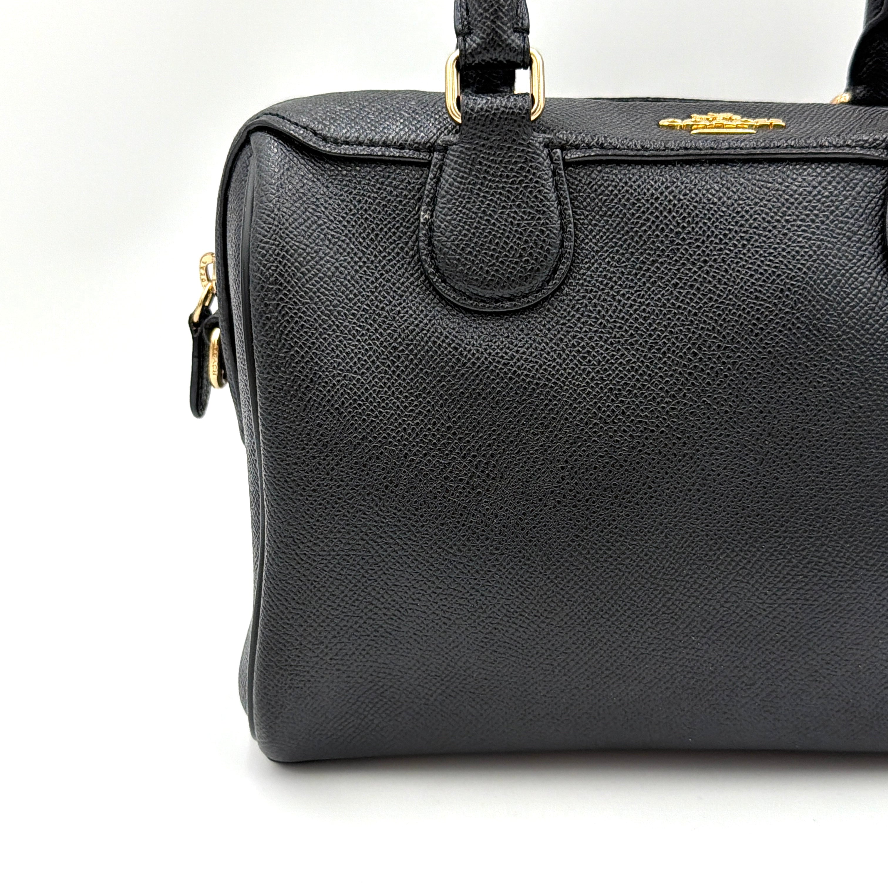 Coach Mini Bennett Boston Bag in black pebbled leather with gold hardware and detachable strap, styled against a clean backdrop.