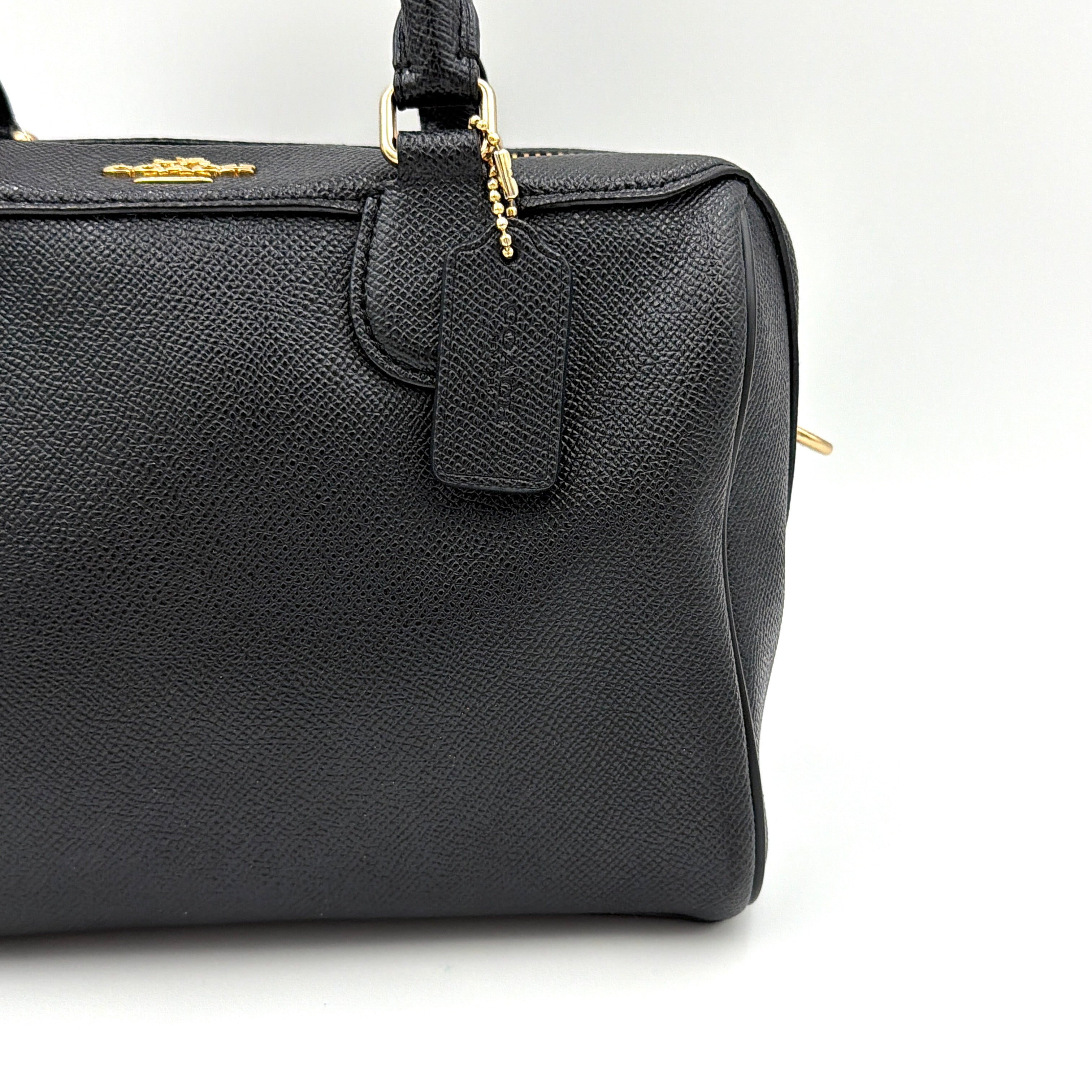 Coach Mini Bennett Boston Bag in black pebbled leather with gold hardware and detachable strap, styled against a clean backdrop.