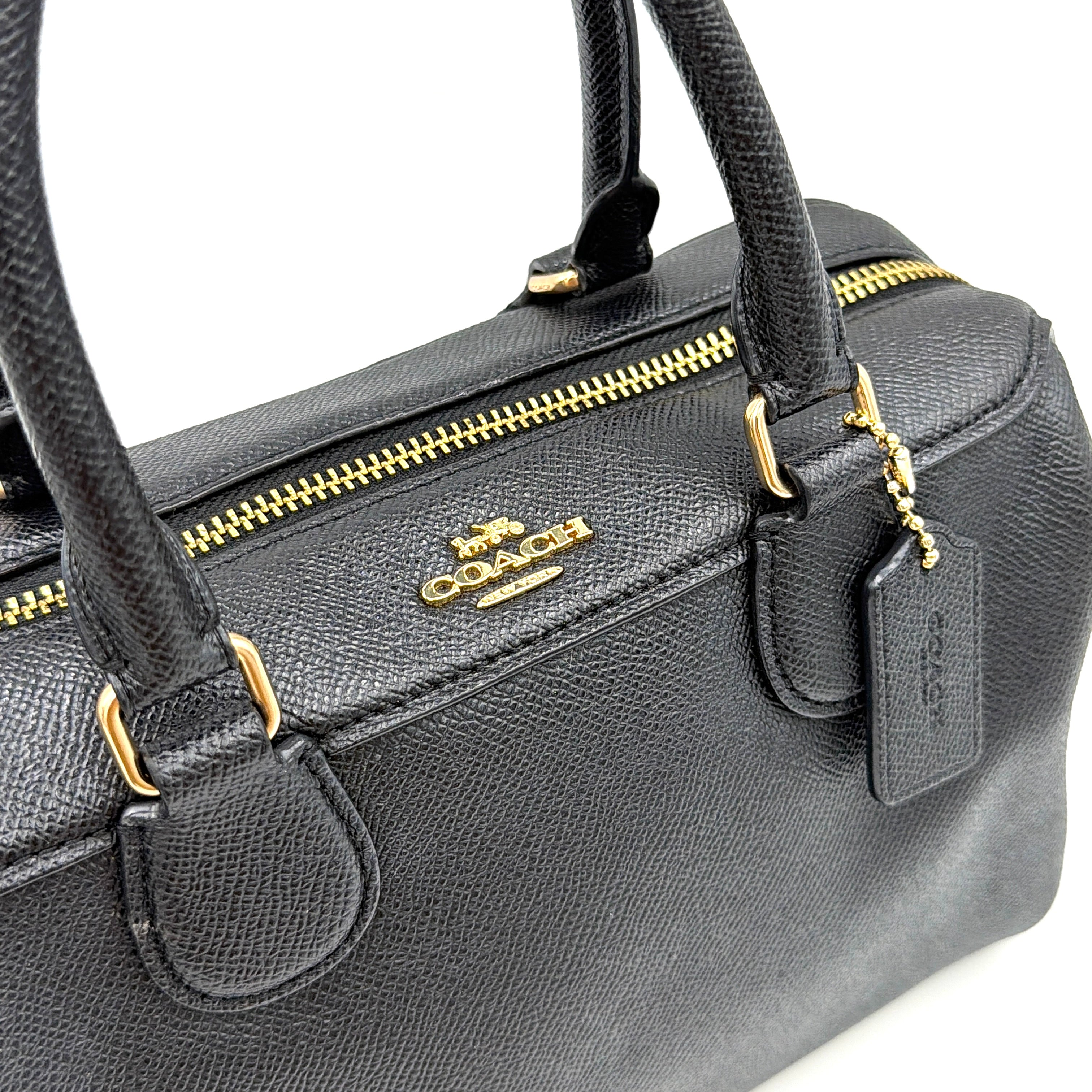 Coach Mini Bennett Boston Bag in black pebbled leather with gold hardware and detachable strap, styled against a clean backdrop.