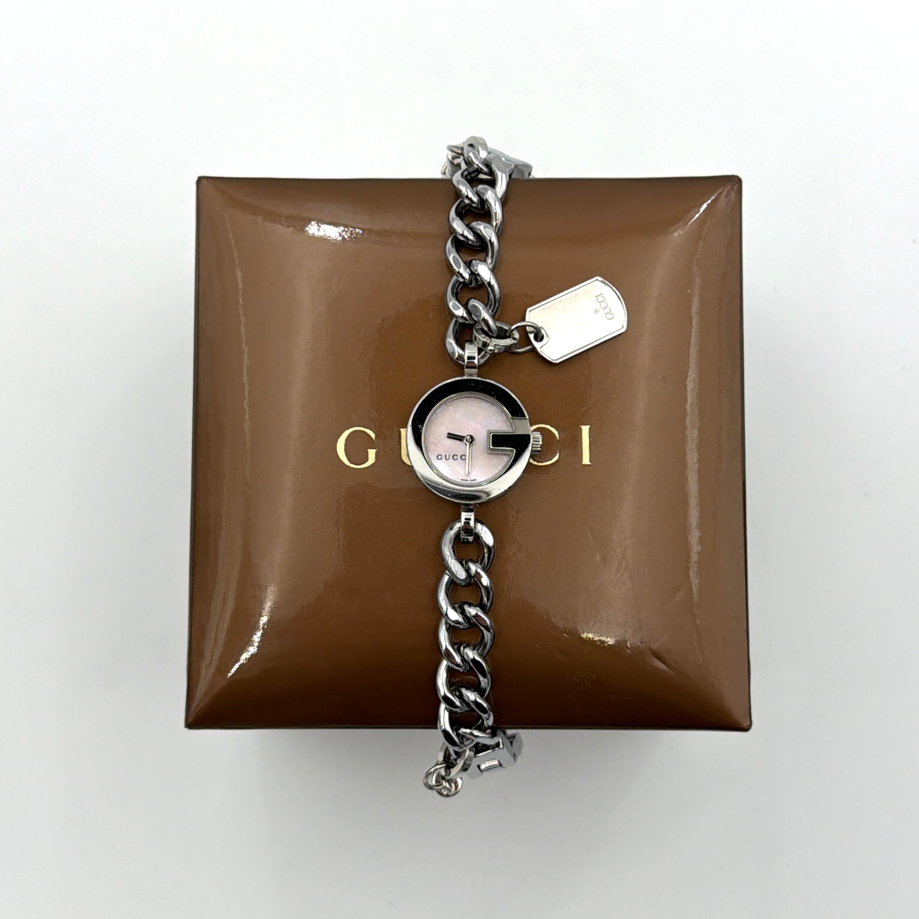 Gucci 107 G Charm Bracelet Watch with silver chunky chain and pink dial, styled on a brown cushion with original Gucci box.