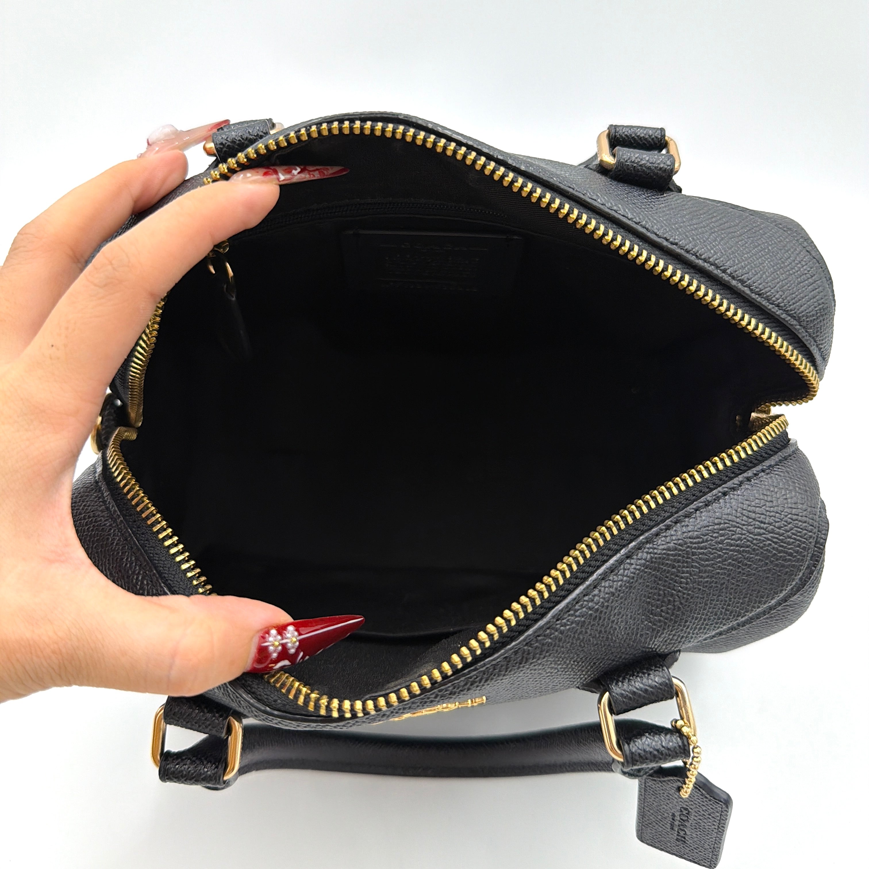 Coach Mini Bennett Boston Bag in black pebbled leather with gold hardware and detachable strap, styled against a clean backdrop.