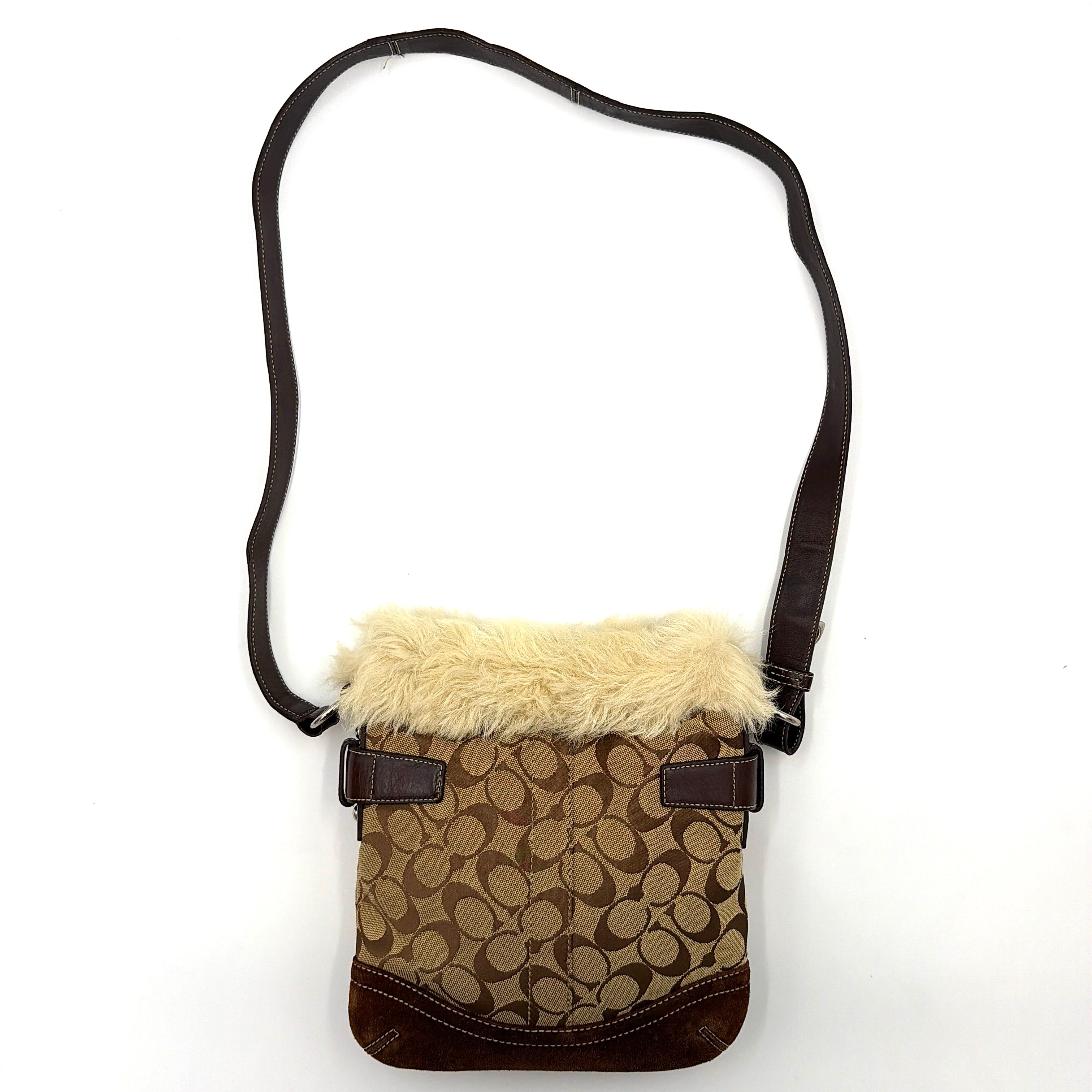 Coach Signature canvas crossbody bag in brown and beige with cream faux fur trim and leather buckle accents, shown with adjustable strap.