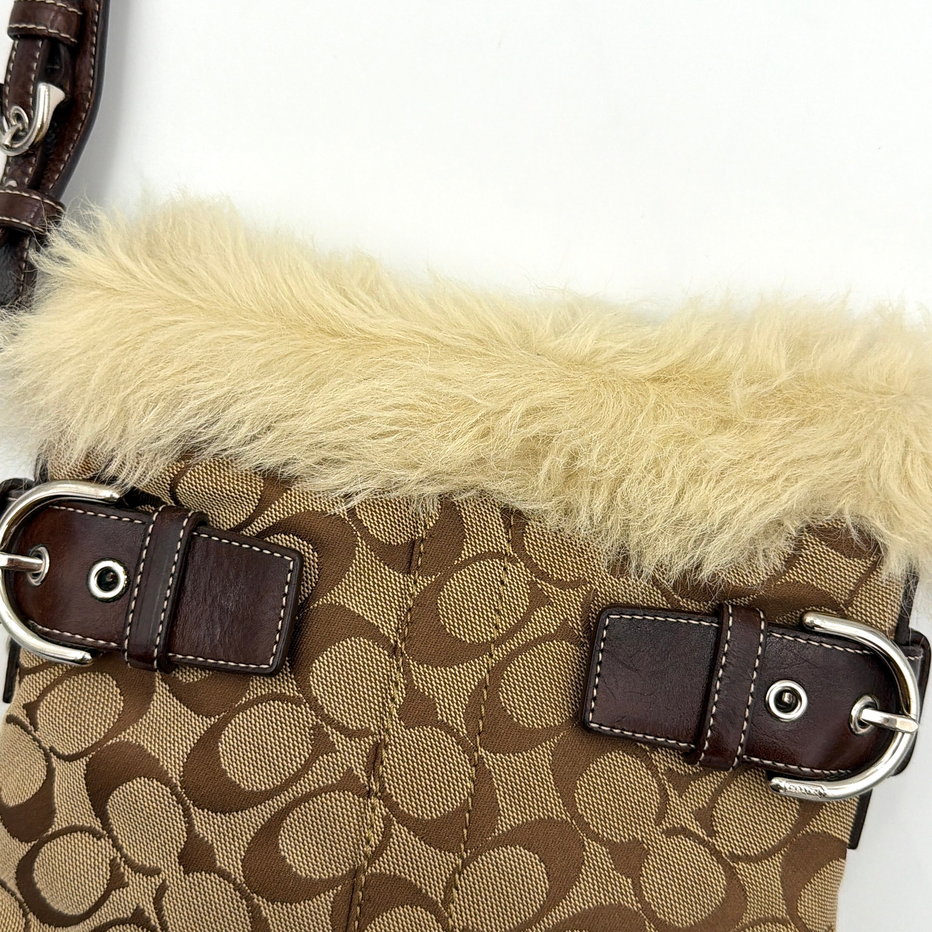 Coach Signature canvas crossbody bag in brown and beige with cream faux fur trim and leather buckle accents, shown with adjustable strap.