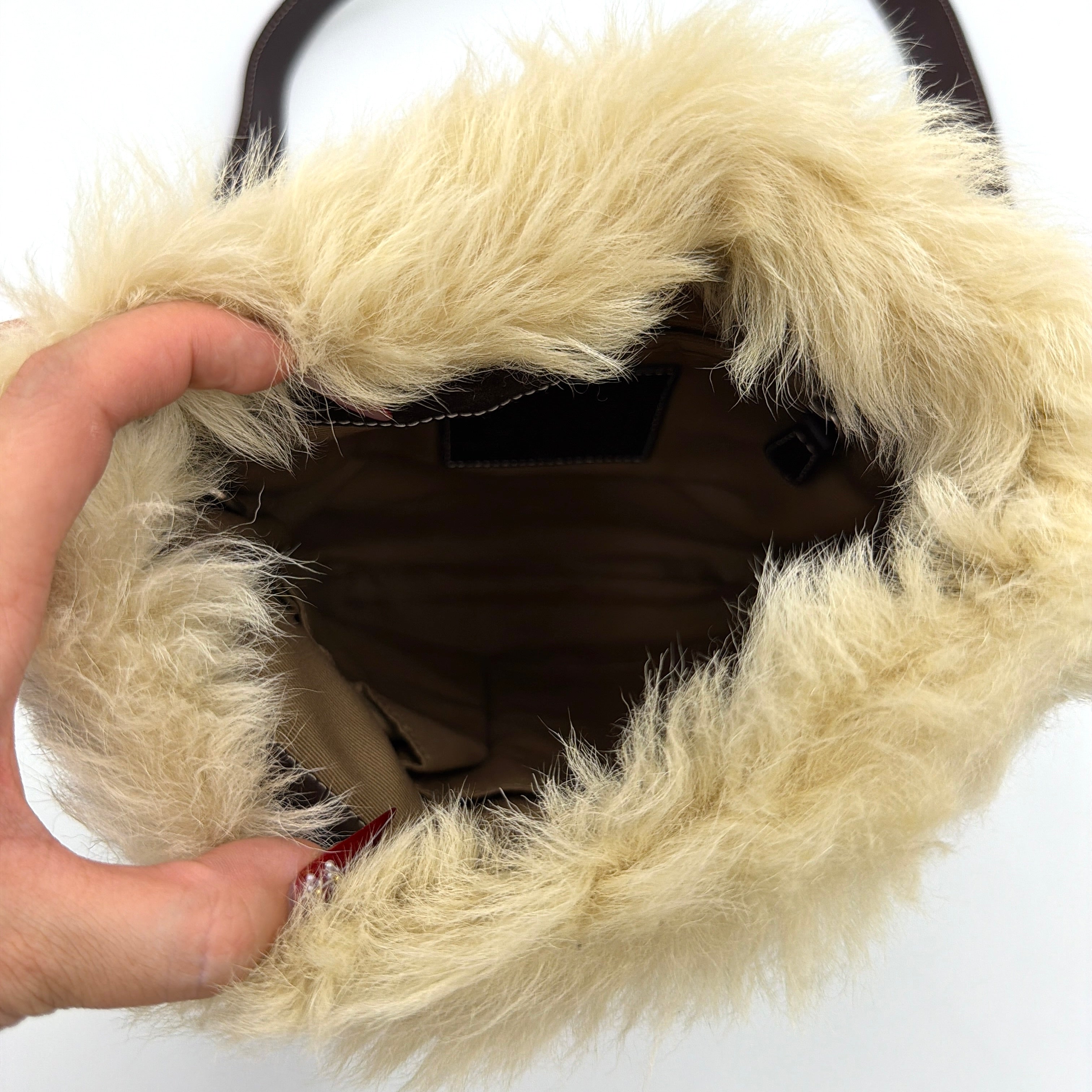 Coach Signature canvas crossbody bag in brown and beige with cream faux fur trim and leather buckle accents, shown with adjustable strap.