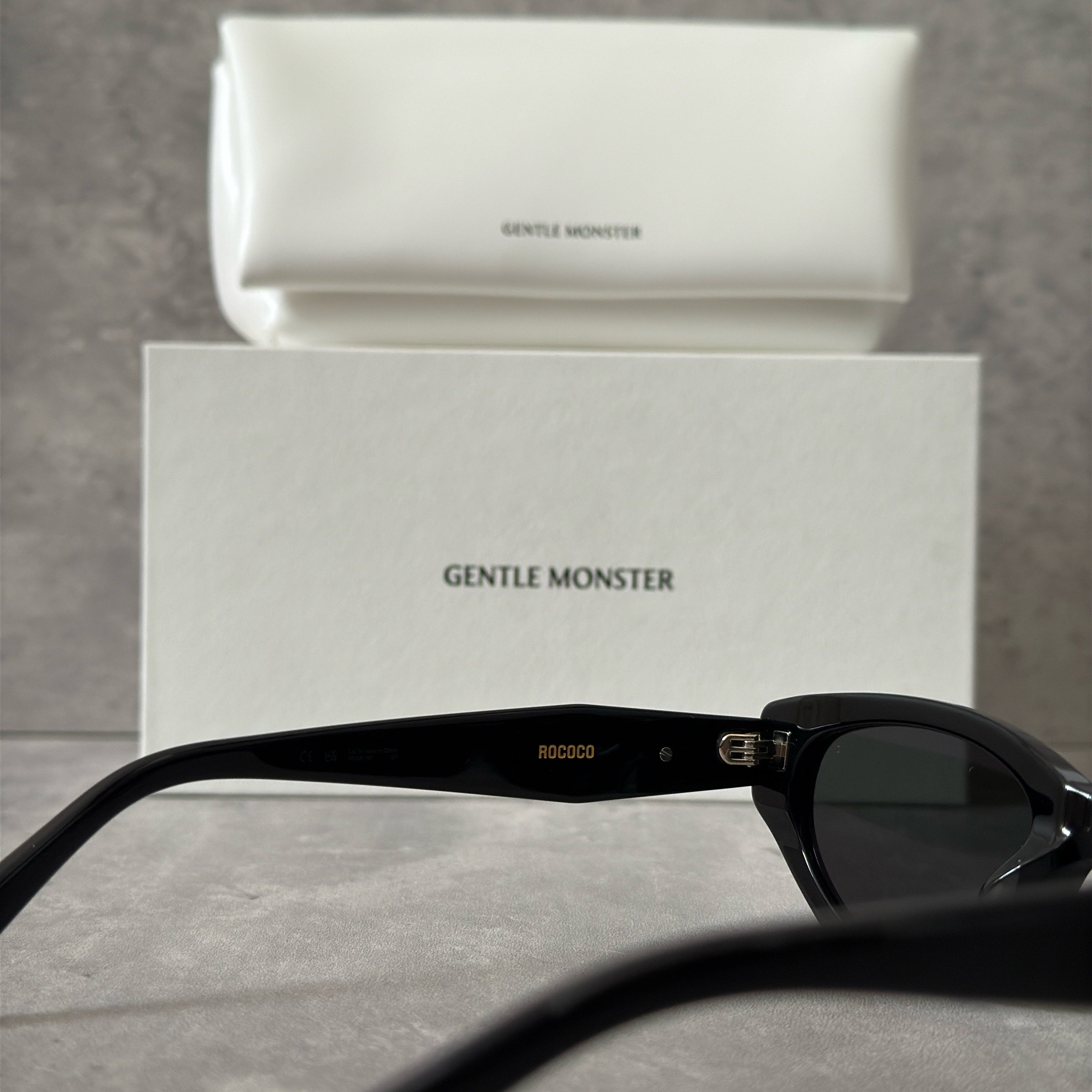 Gentle Monster ROCOCO - 01 black tinted sunglasses with a sleek acetate frame and gold-tone logo on temples.