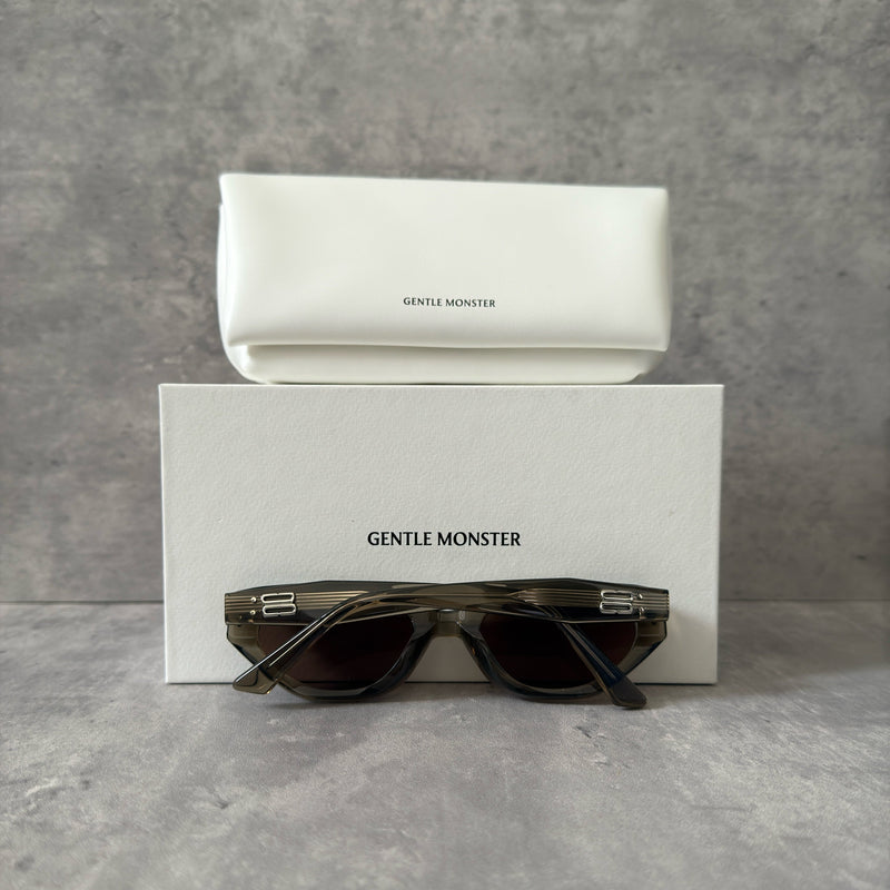 Gentle Monster ROCOCO KC6 sunglasses in translucent smoky brown acetate, featuring a bold sculpted design, tinted brown lenses, and signature metal temple detailing.