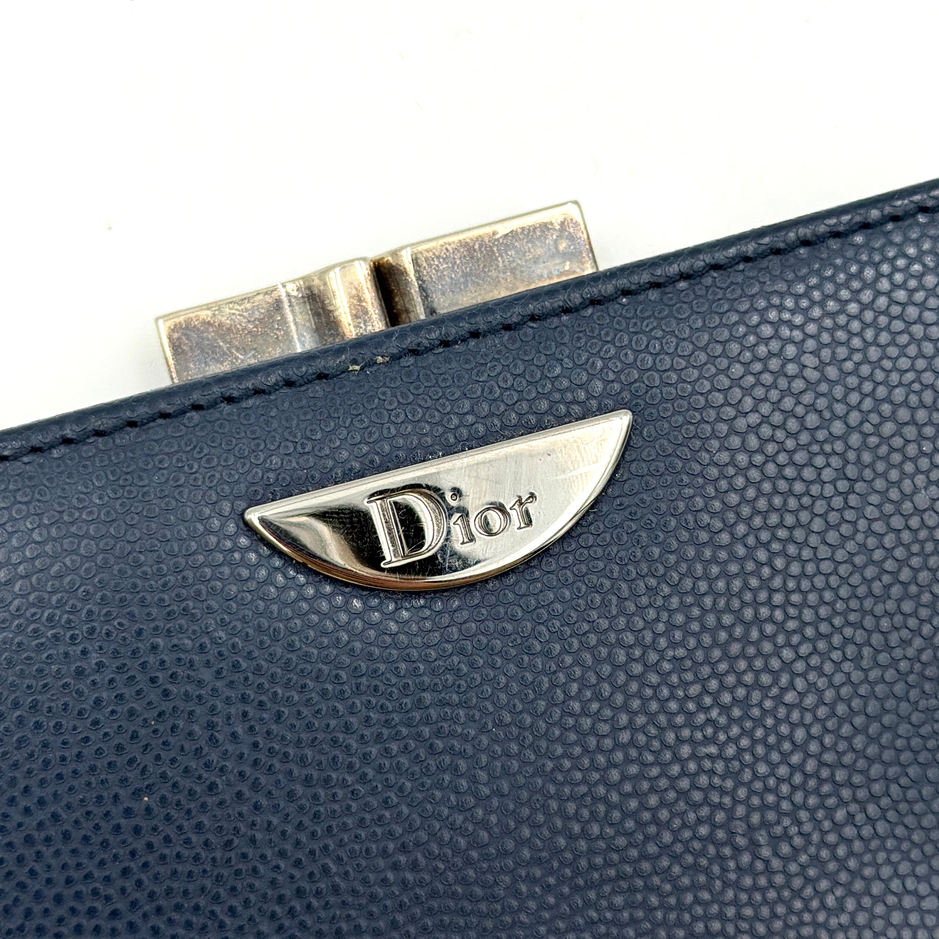 Dior compact navy blue leather wallet with silver-tone logo plaque and kiss-lock clasp, showcased against a clean background.