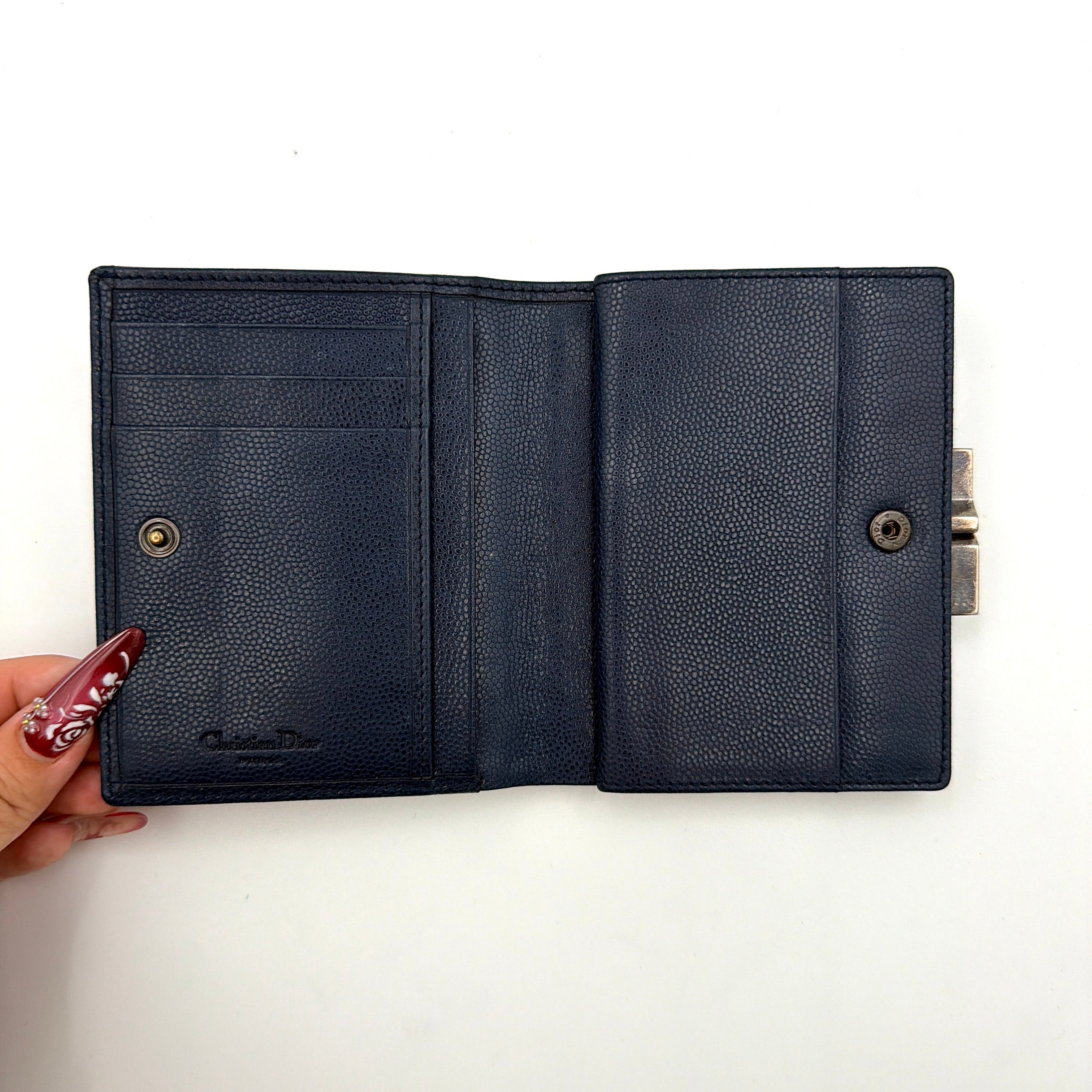 Dior compact navy blue leather wallet with silver-tone logo plaque and kiss-lock clasp, showcased against a clean background.