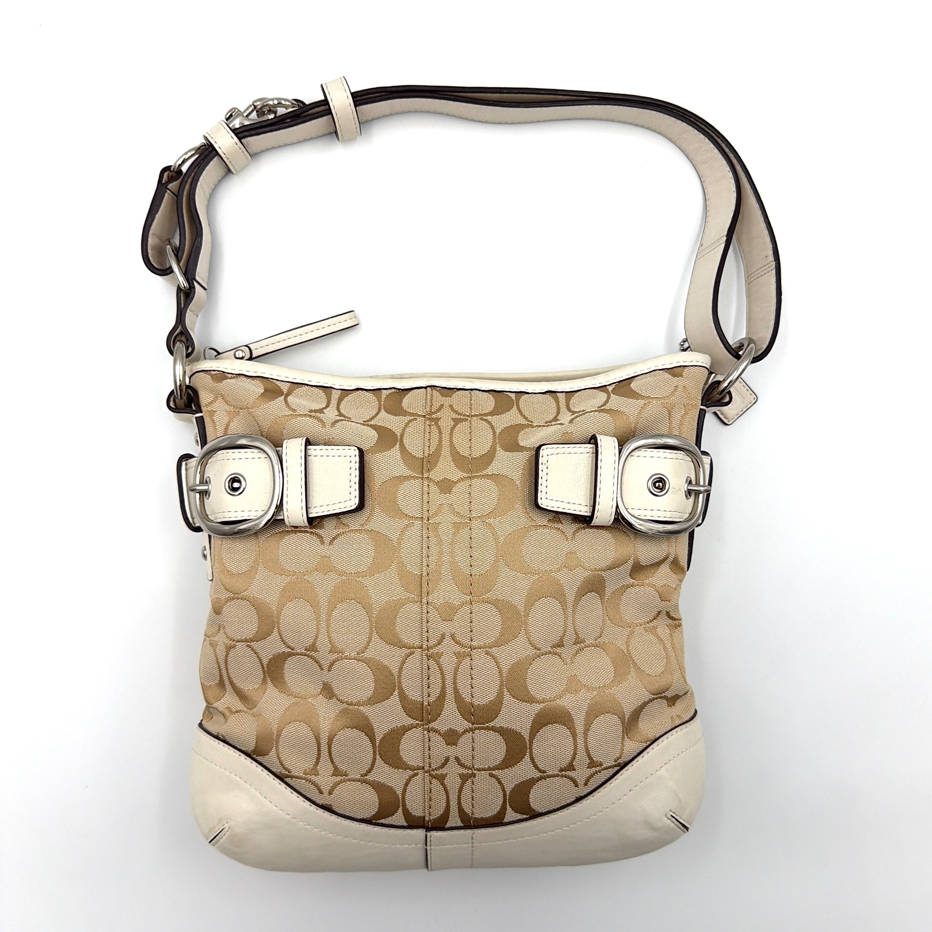 Coach beige and white signature canvas shoulder bag with white leather trim, silver buckles, and adjustable strap on display.