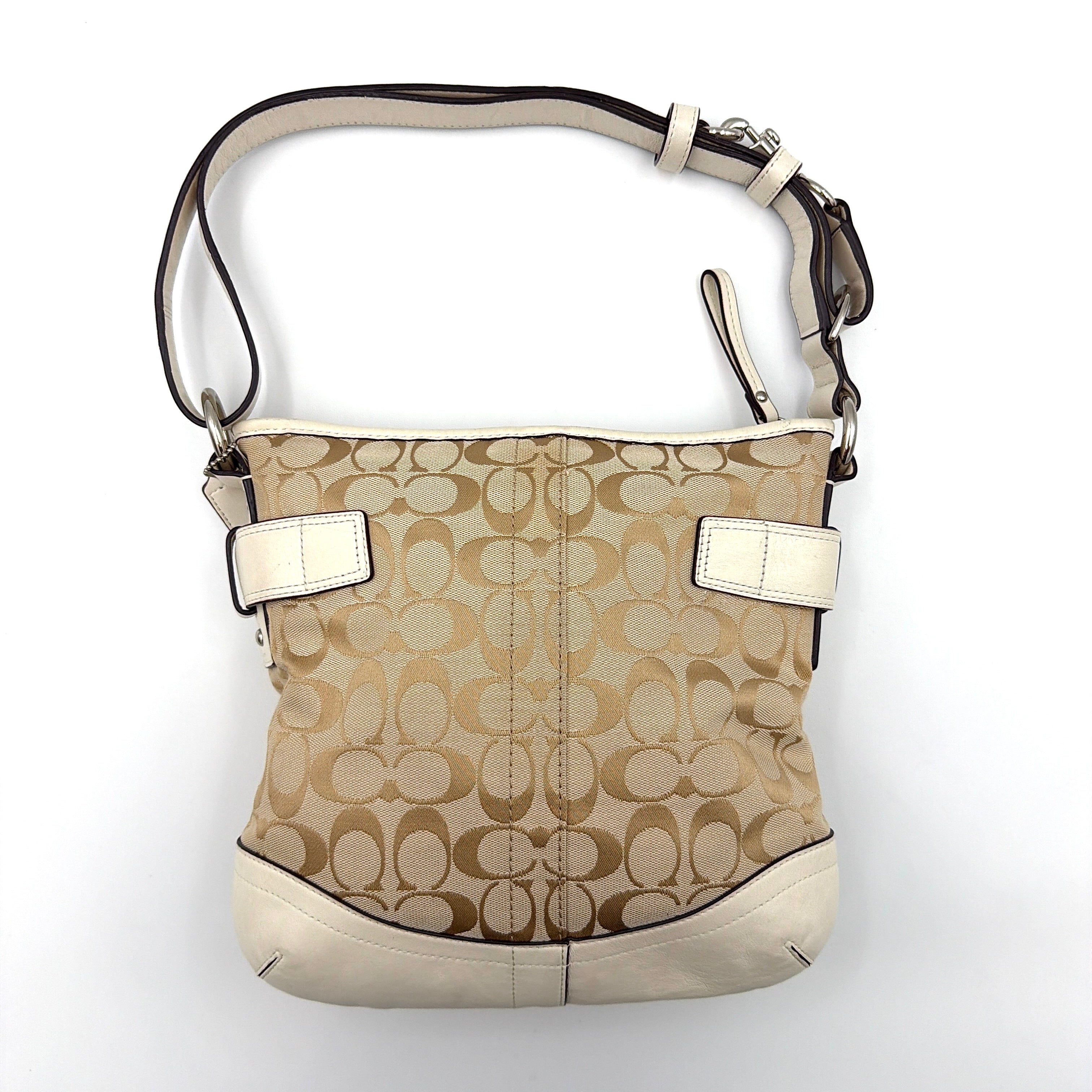 Coach beige and white signature canvas shoulder bag with white leather trim, silver buckles, and adjustable strap on display.