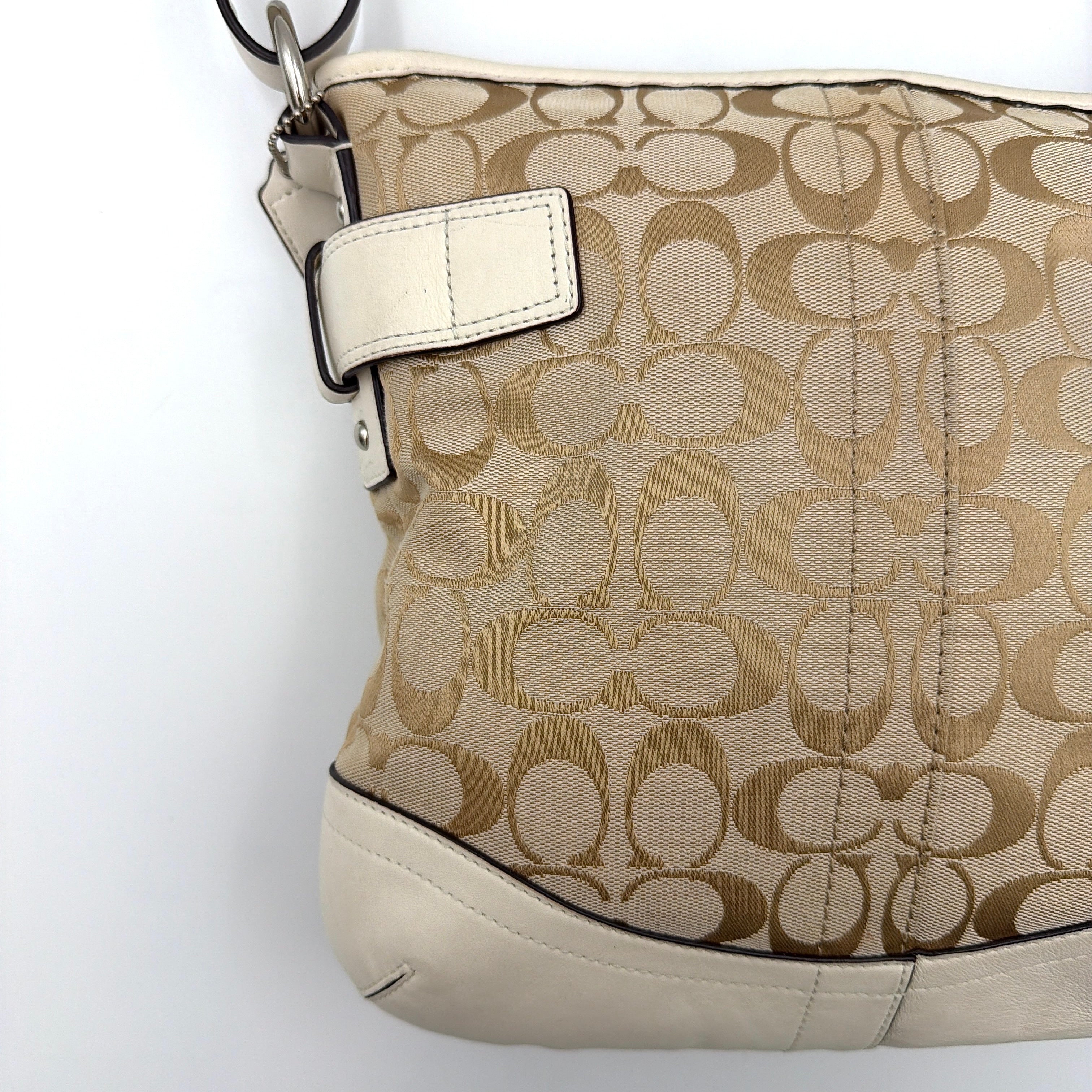 Coach beige and white signature canvas shoulder bag with white leather trim, silver buckles, and adjustable strap on display.