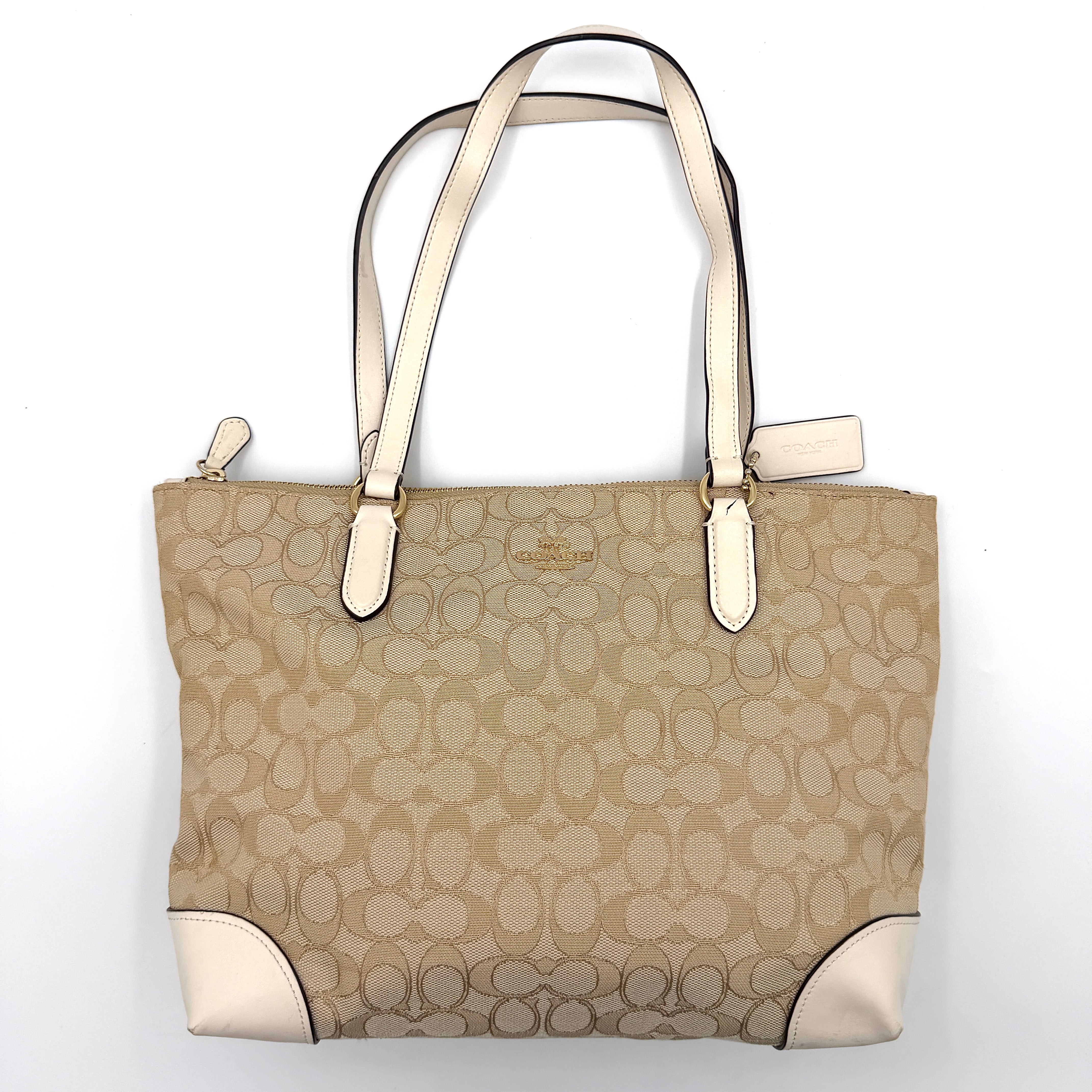 Coach Signature Zip Top Tote Bag in beige canvas with white leather trim and double handles, featuring the signature monogram print.
