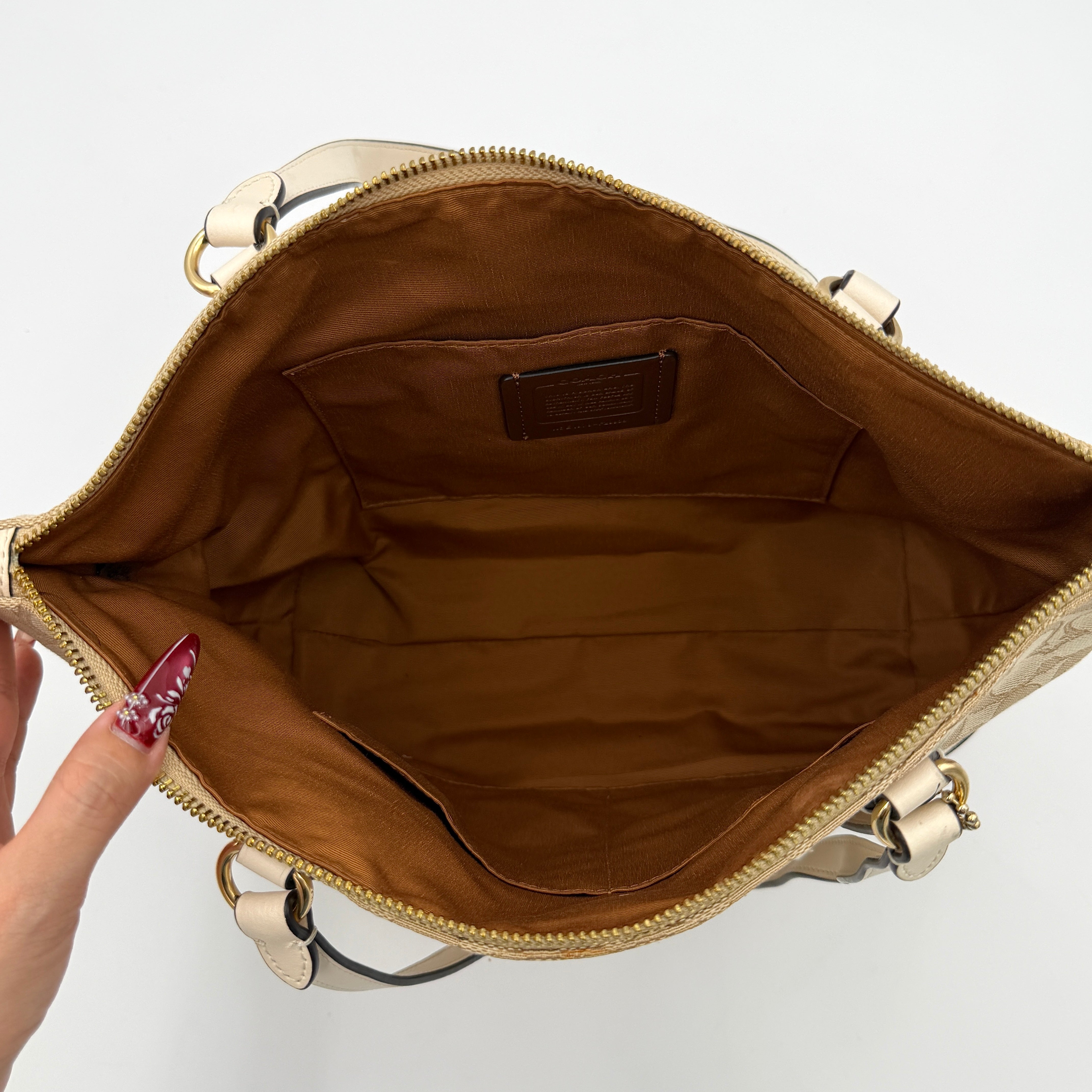 Coach Signature Zip Top Tote Bag in beige canvas with white leather trim and double handles, featuring the signature monogram print.