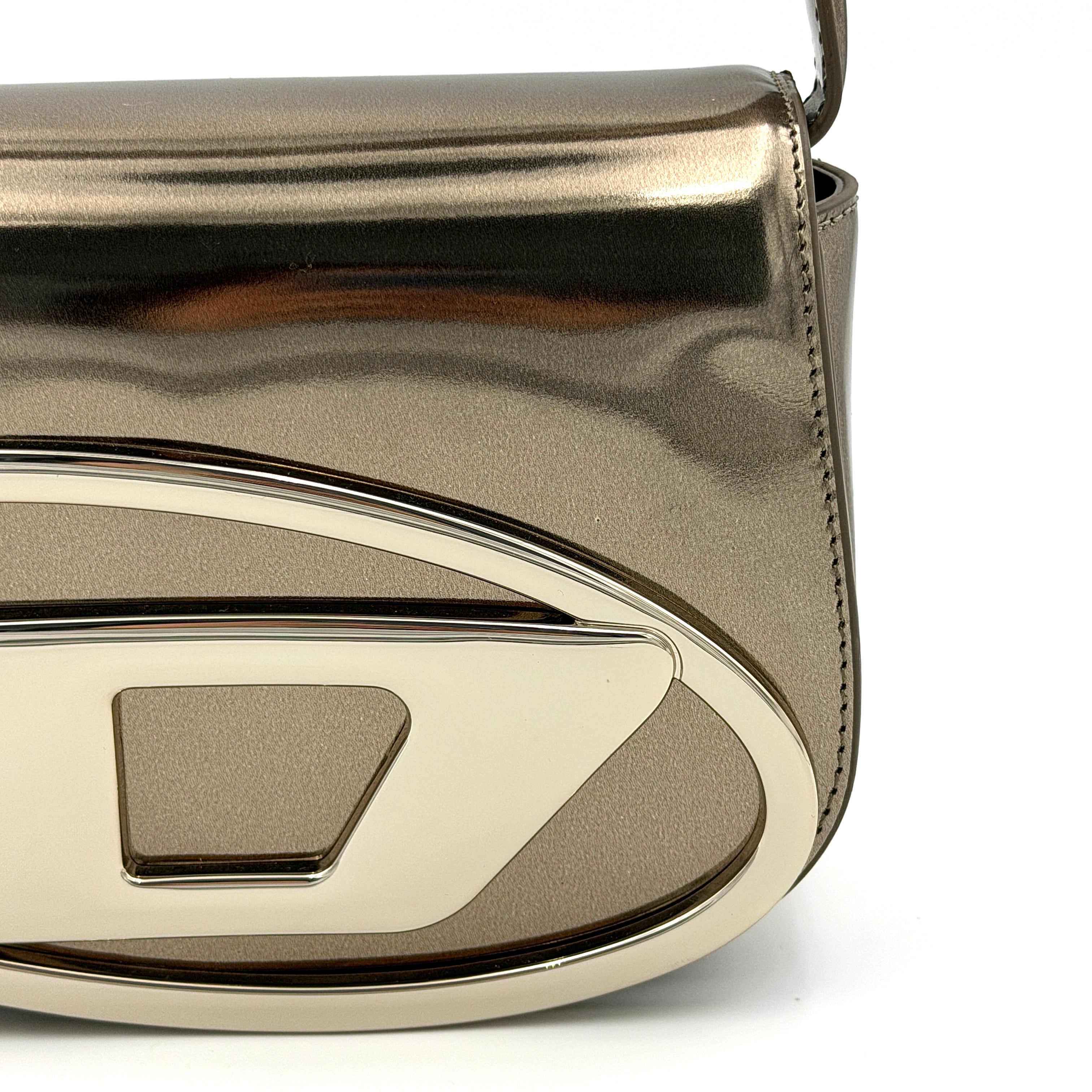 Diesel 1DR metallic silver shoulder bag with oversized chrome D-logo plaque, top handle, and detachable strap displayed against a white background.