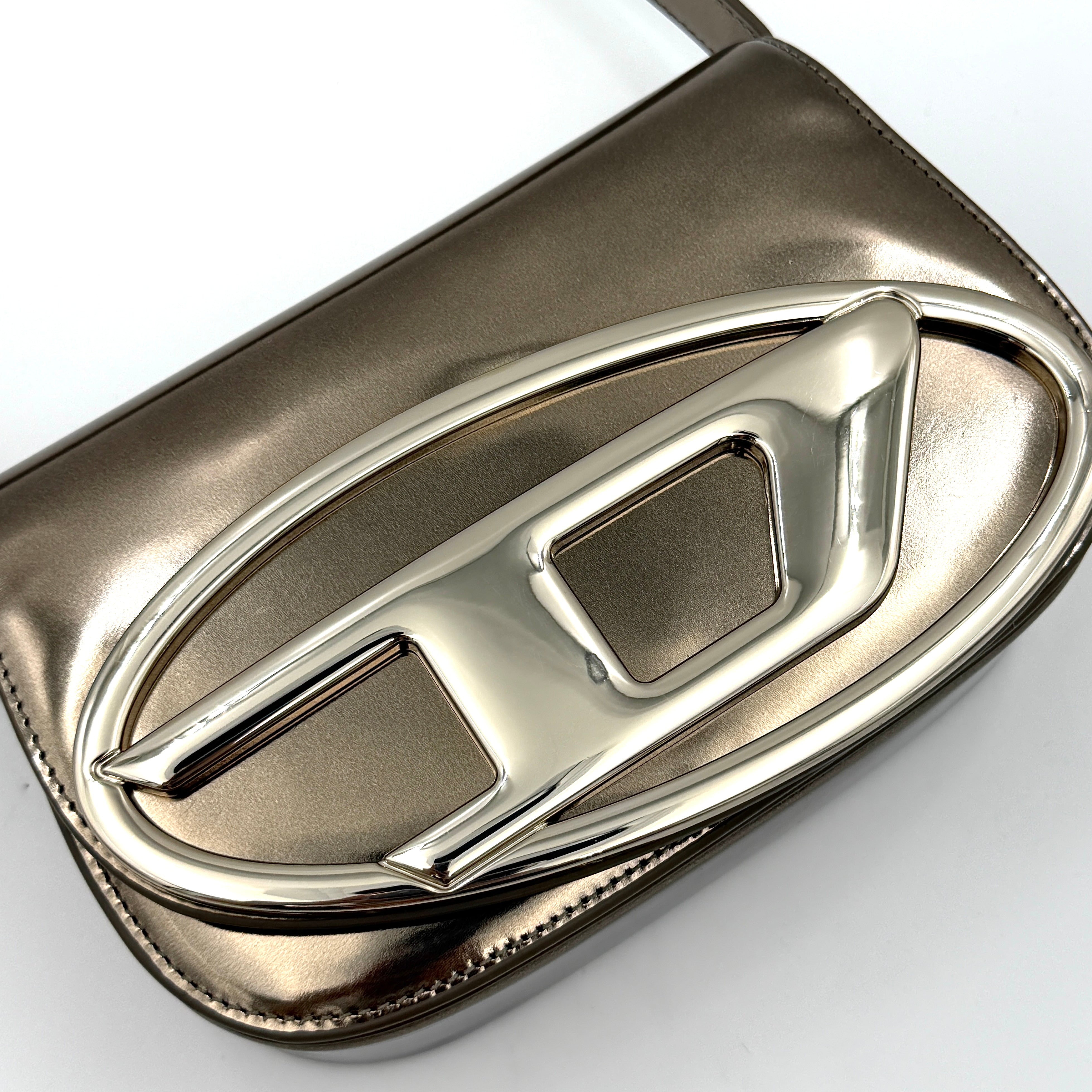Diesel 1DR metallic silver shoulder bag with oversized chrome D-logo plaque, top handle, and detachable strap displayed against a white background.