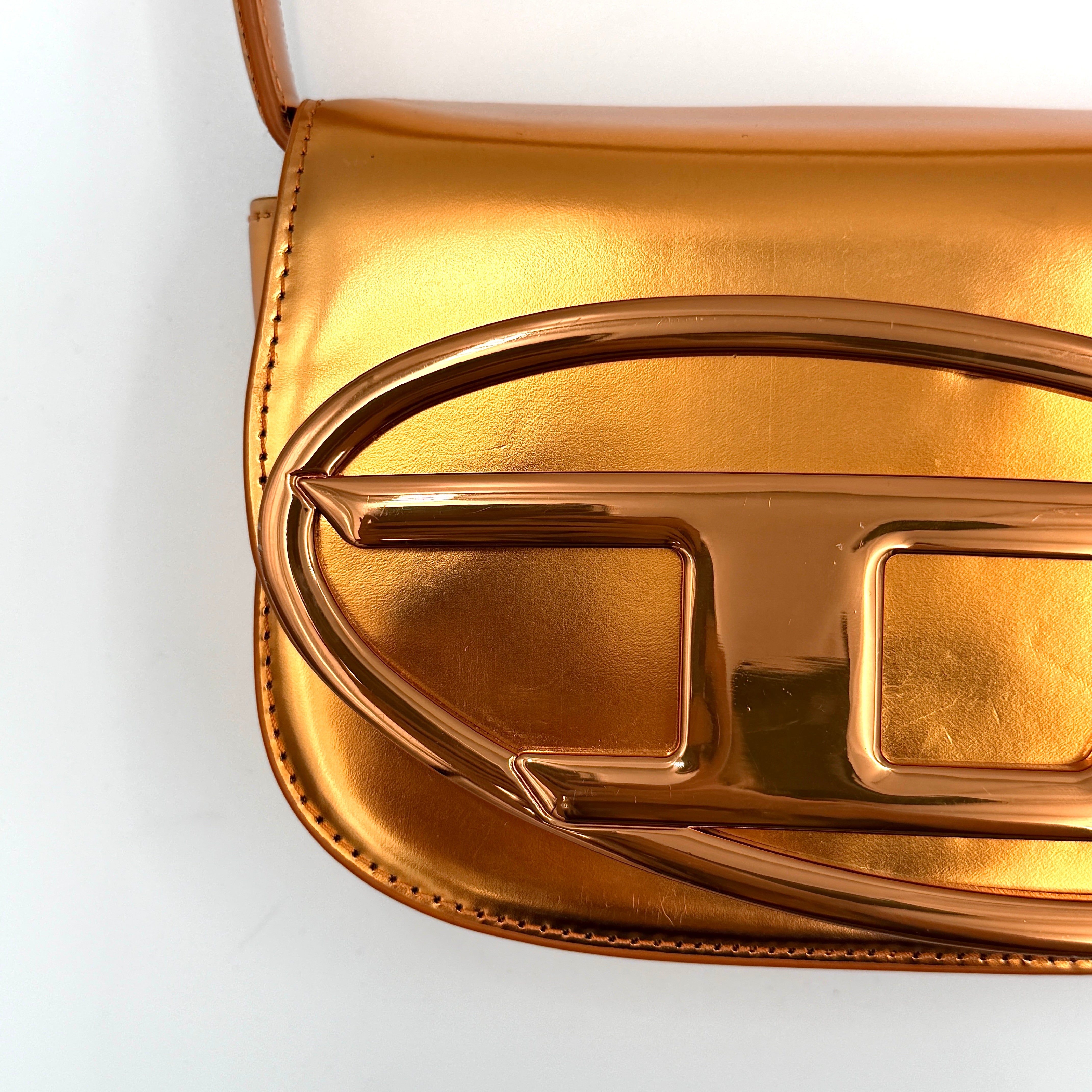 A Diesel 2Way 1DR Shoulder Bag in striking metallic gold with an embossed logo and detachable strap, displayed alongside its accessories.