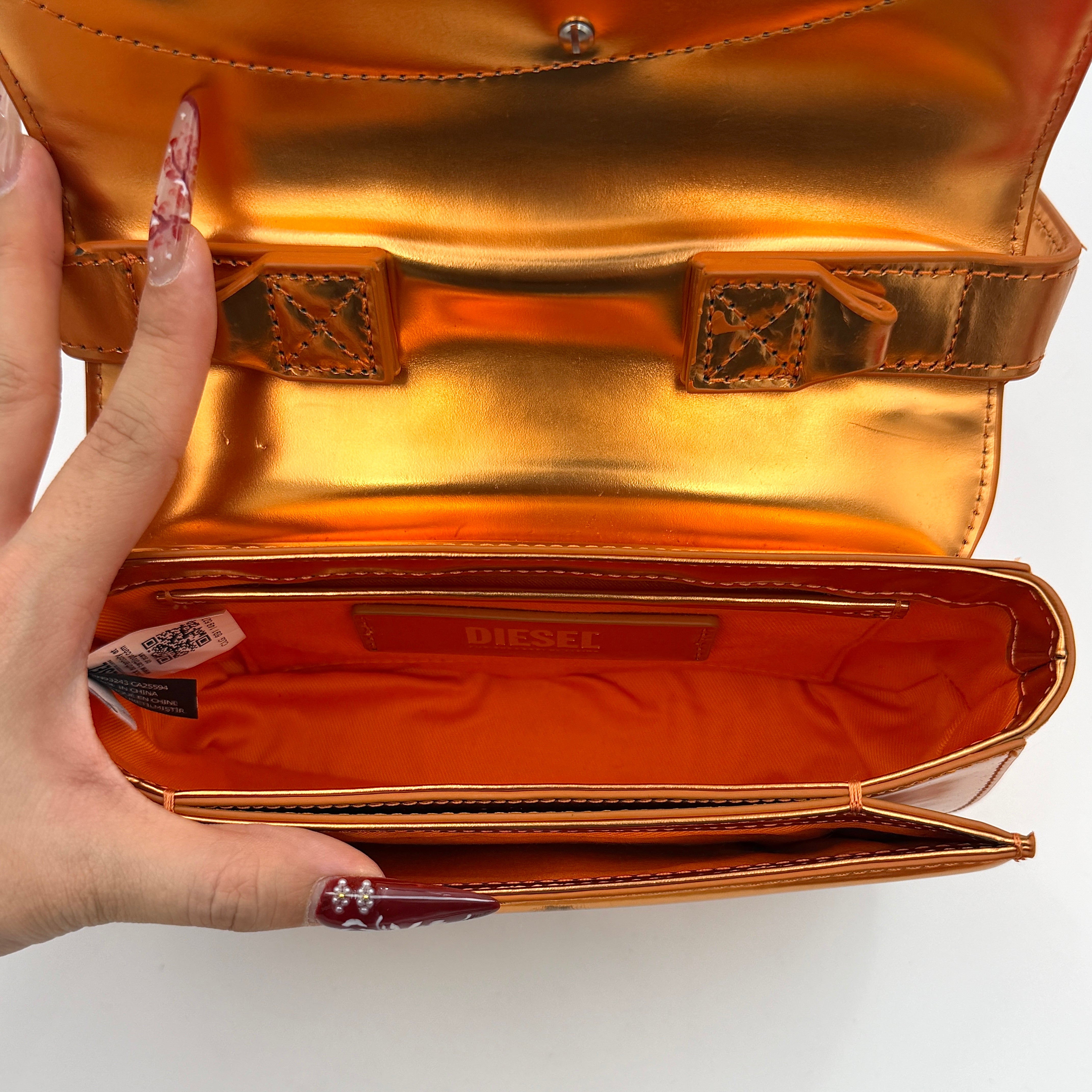 A Diesel 2Way 1DR Shoulder Bag in striking metallic gold with an embossed logo and detachable strap, displayed alongside its accessories.