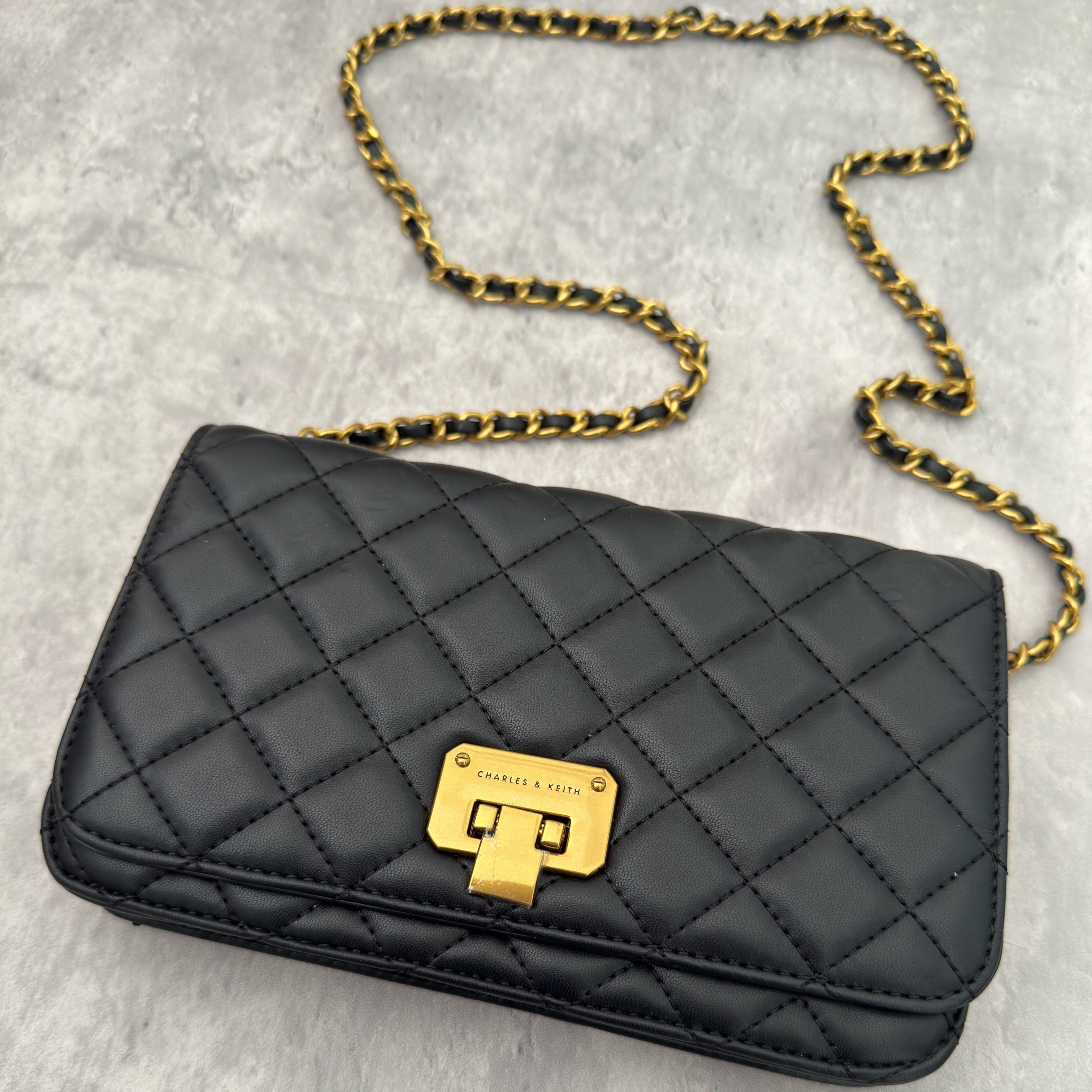 Charles & Keith Cressida Quilted Push-Lock Clutch Bag in black faux leather with gold-tone chain strap and secure push-lock closure.