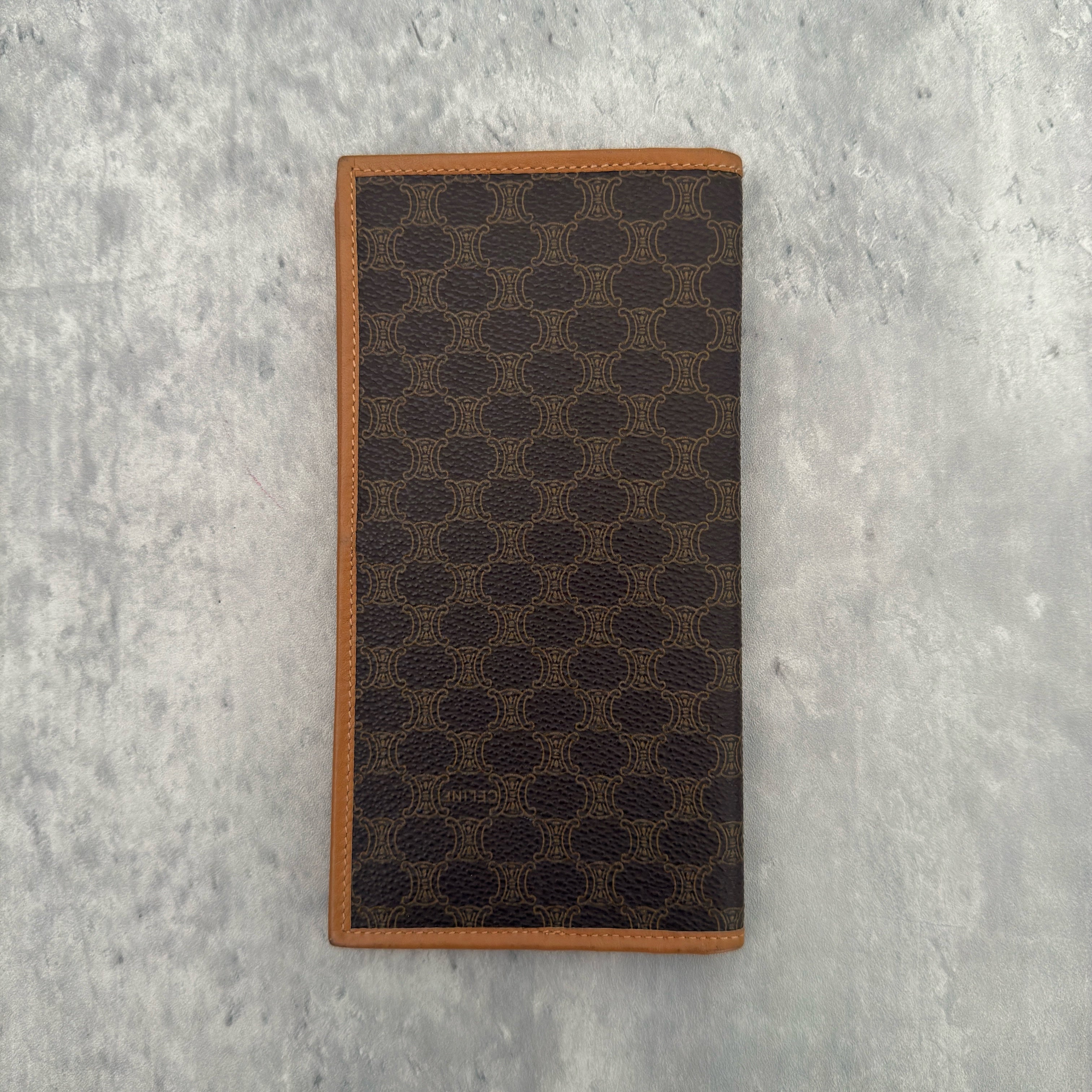 Celine Macadam Triomphe Canvas Long Wallet in brown monogram canvas with tan leather trim, featuring a bifold design with multiple compartments and a snap-button coin pocket.