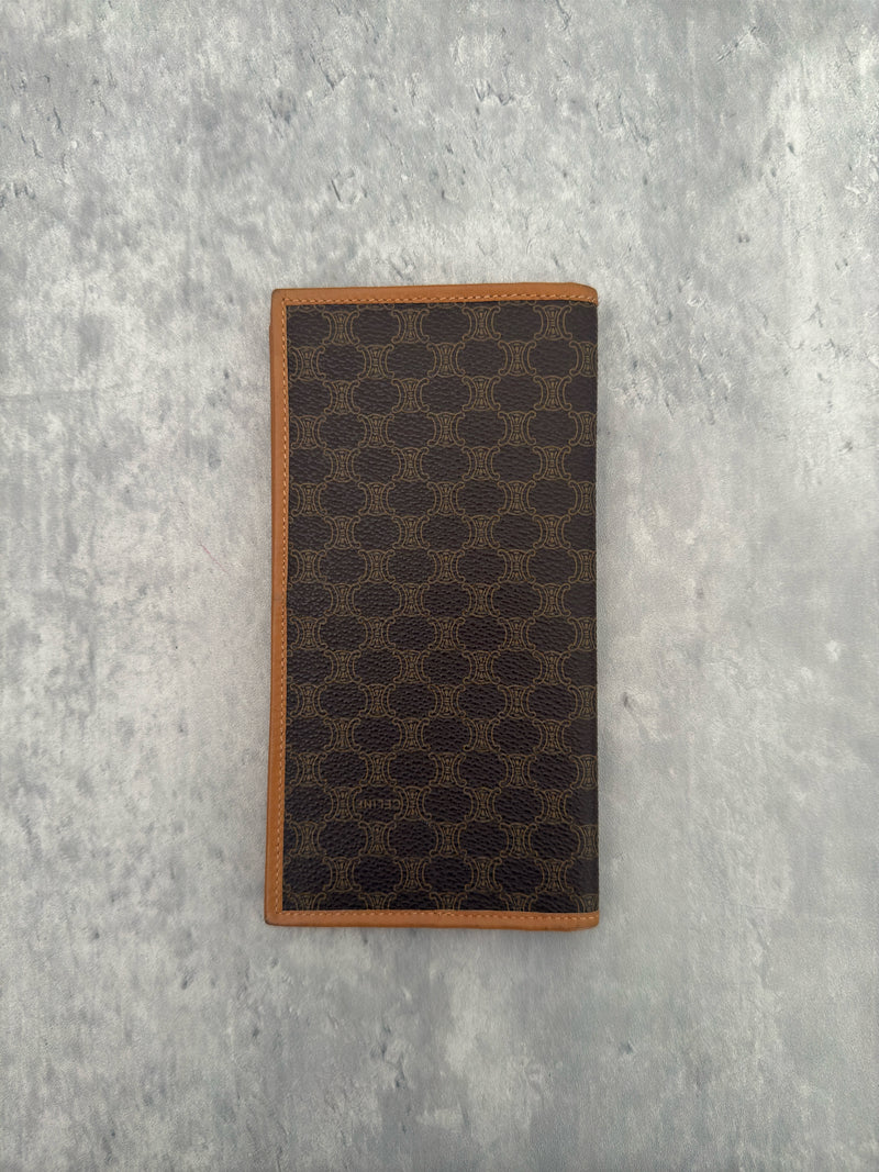 Celine Macadam Triomphe Canvas Long Wallet in brown monogram canvas with tan leather trim, featuring a bifold design with multiple compartments and a snap-button coin pocket.