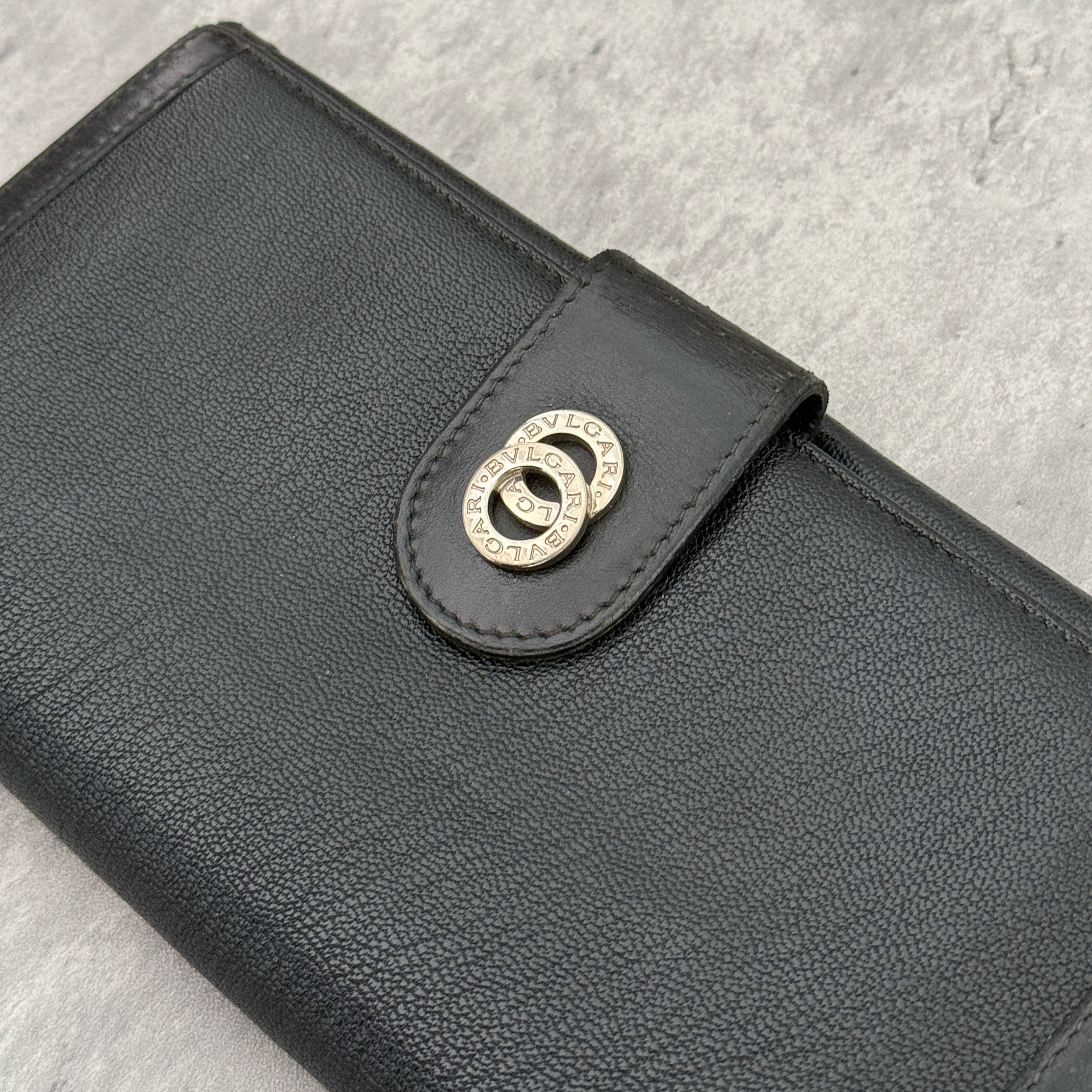 Bvlgari Doppio Tondo Bifold Long Wallet in black leather, featuring a silver-tone logo clasp, red fabric interior, and multiple compartments.