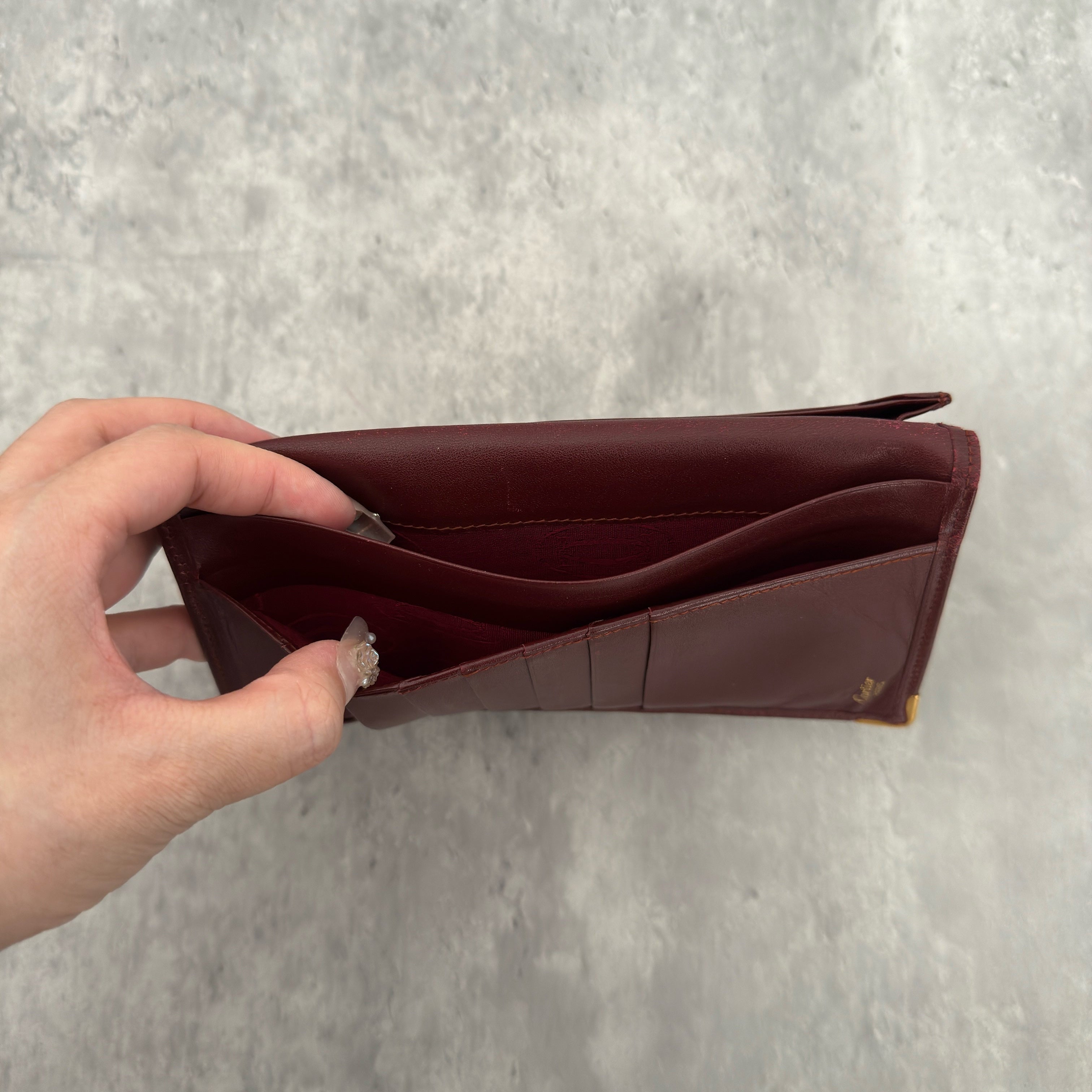 Cartier Must De Cartier Burgundy Long Wallet in burgundy leather with gold-tone corner accents and multiple compartments.