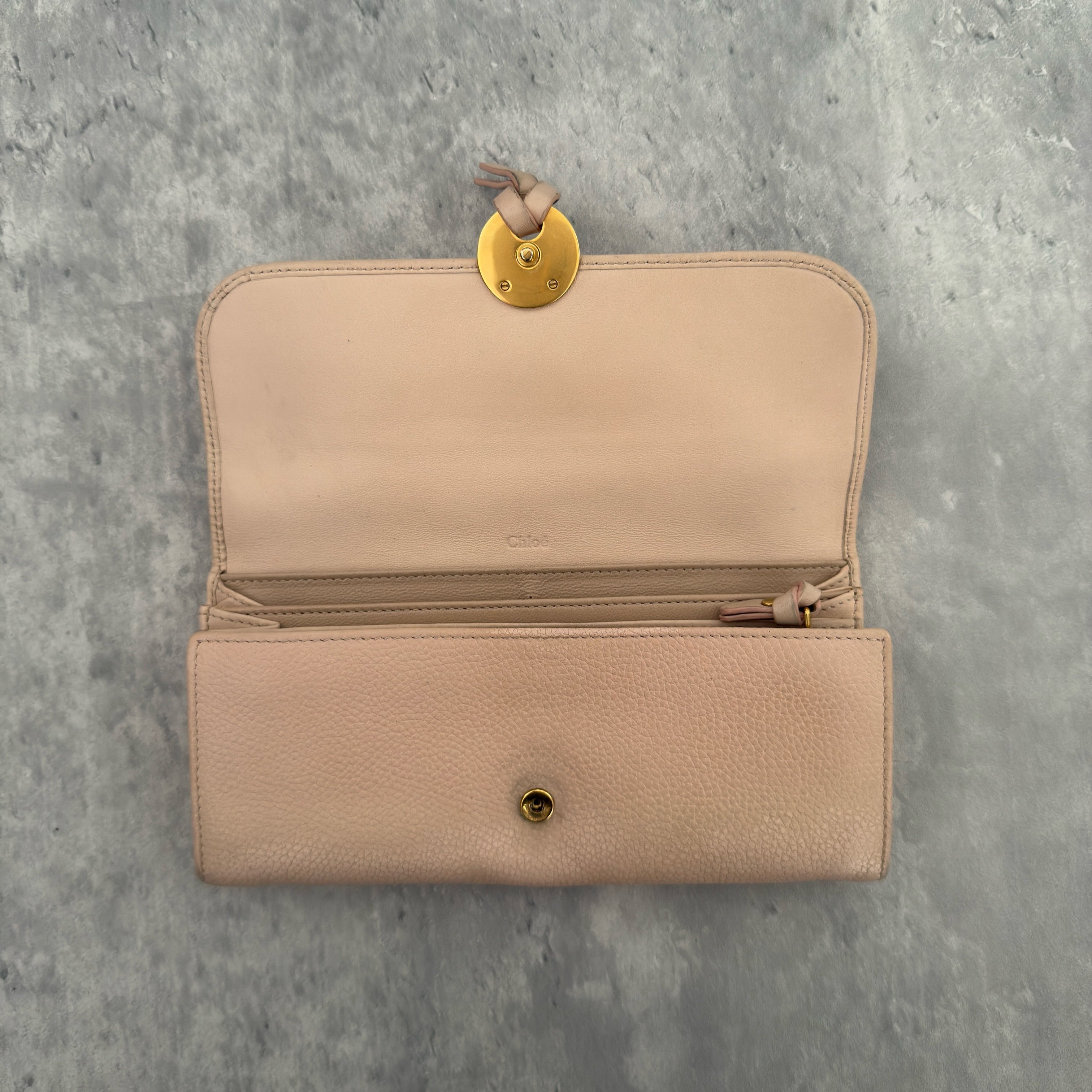 Chloe Grained Smooth Calfskin Indy Long Wallet in Light Pink, featuring a gold-tone circular medallion closure with leather tie detail, crafted from a mix of grained and smooth calfskin leather.