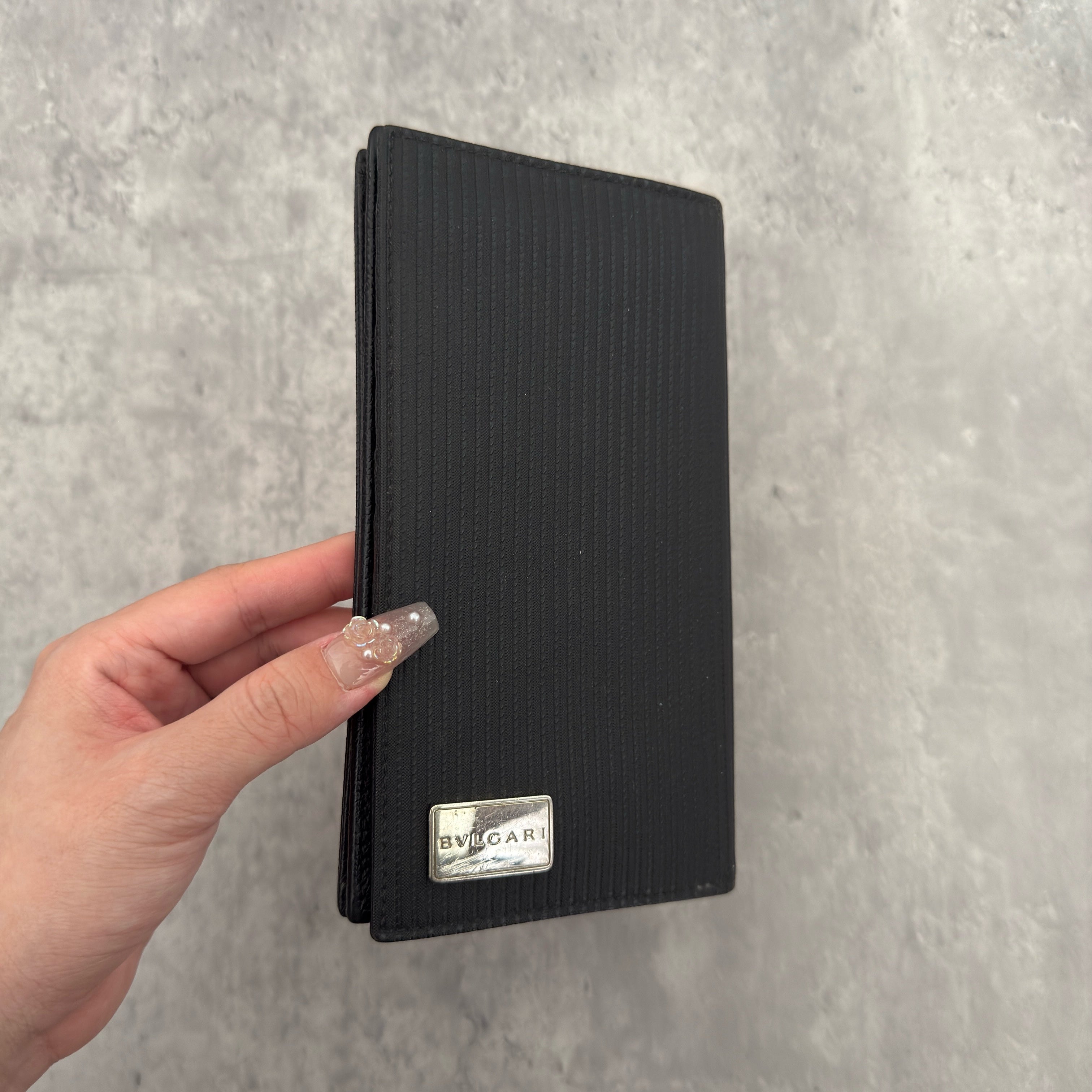 Bvlgari Ribbed Nylon Long Bifold Wallet in black with a silver-tone metal plaque logo, featuring multiple compartments and a sleek ribbed texture.