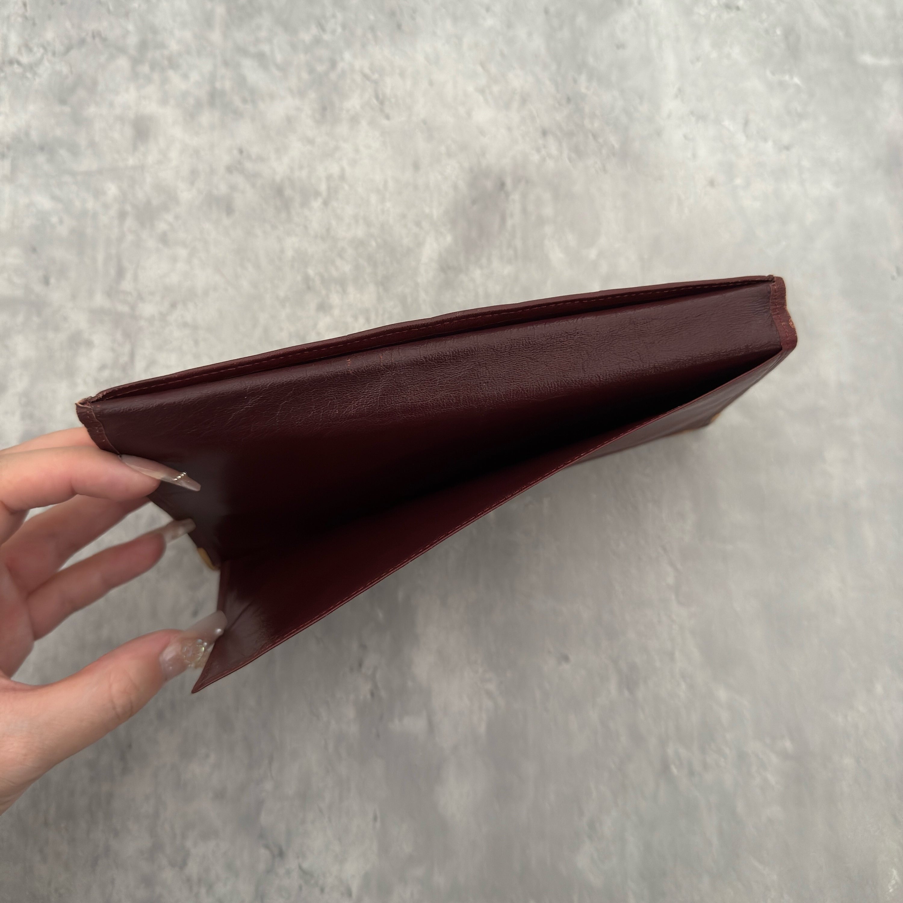 Cartier Must De Cartier Long Wallet in burgundy leather with embossed logo, gold-tone corner accents, and multiple compartments for organised storage.