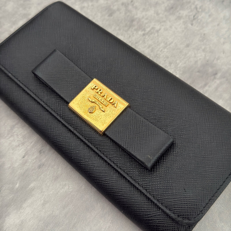 Prada Milano Black Saffiano Leather Ribbon Bow Long Wallet, crafted from textured black Saffiano leather with a gold-tone logo plaque and ribbon bow detail.