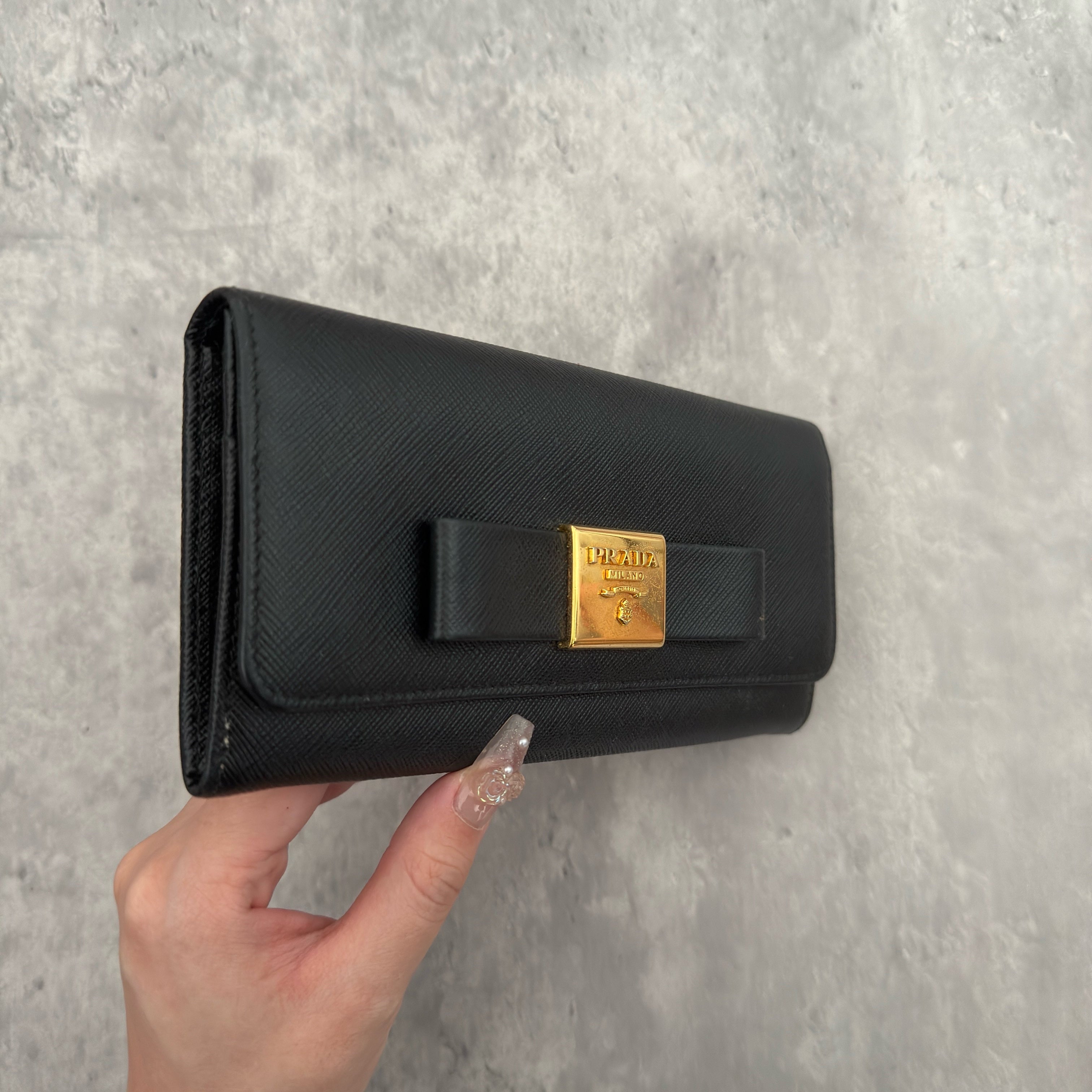 Prada Milano Black Saffiano Leather Ribbon Bow Long Wallet, crafted from textured black Saffiano leather with a gold-tone logo plaque and ribbon bow detail.